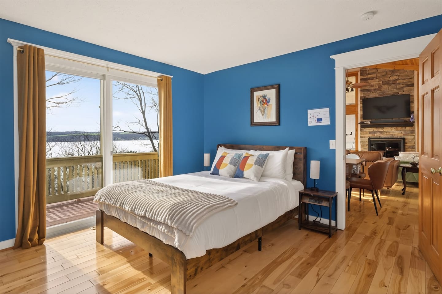 Bright blue master bedroom with stylish artwork, Smart TV, and private balcony access—wake up to peaceful lake views, step outside to sip your morning coffee, and enjoy a calm, relaxing retreat filled with light and comfort