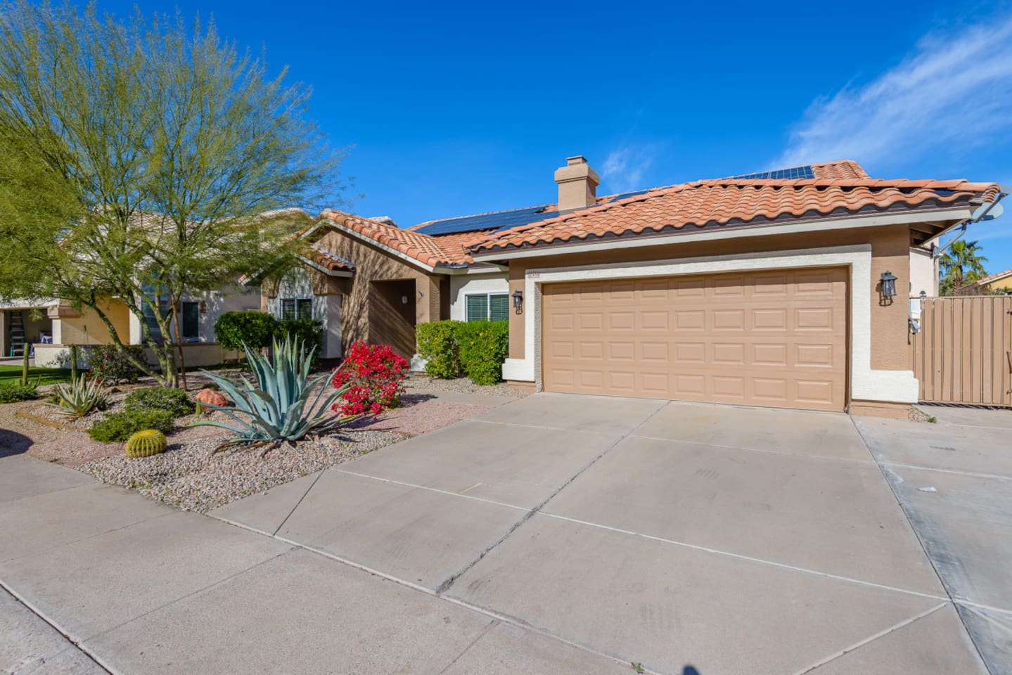 Front entry view with mature desert landscaping, paved walkway, and easy garage access.
