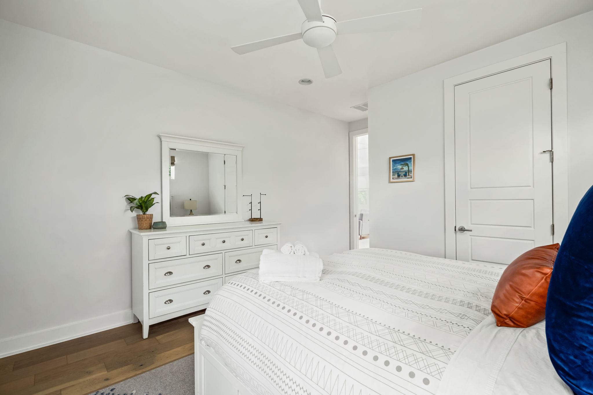 Bright bedroom featuring a queen bed with colorful accent pillows, a spacious dresser, and easy closet access.