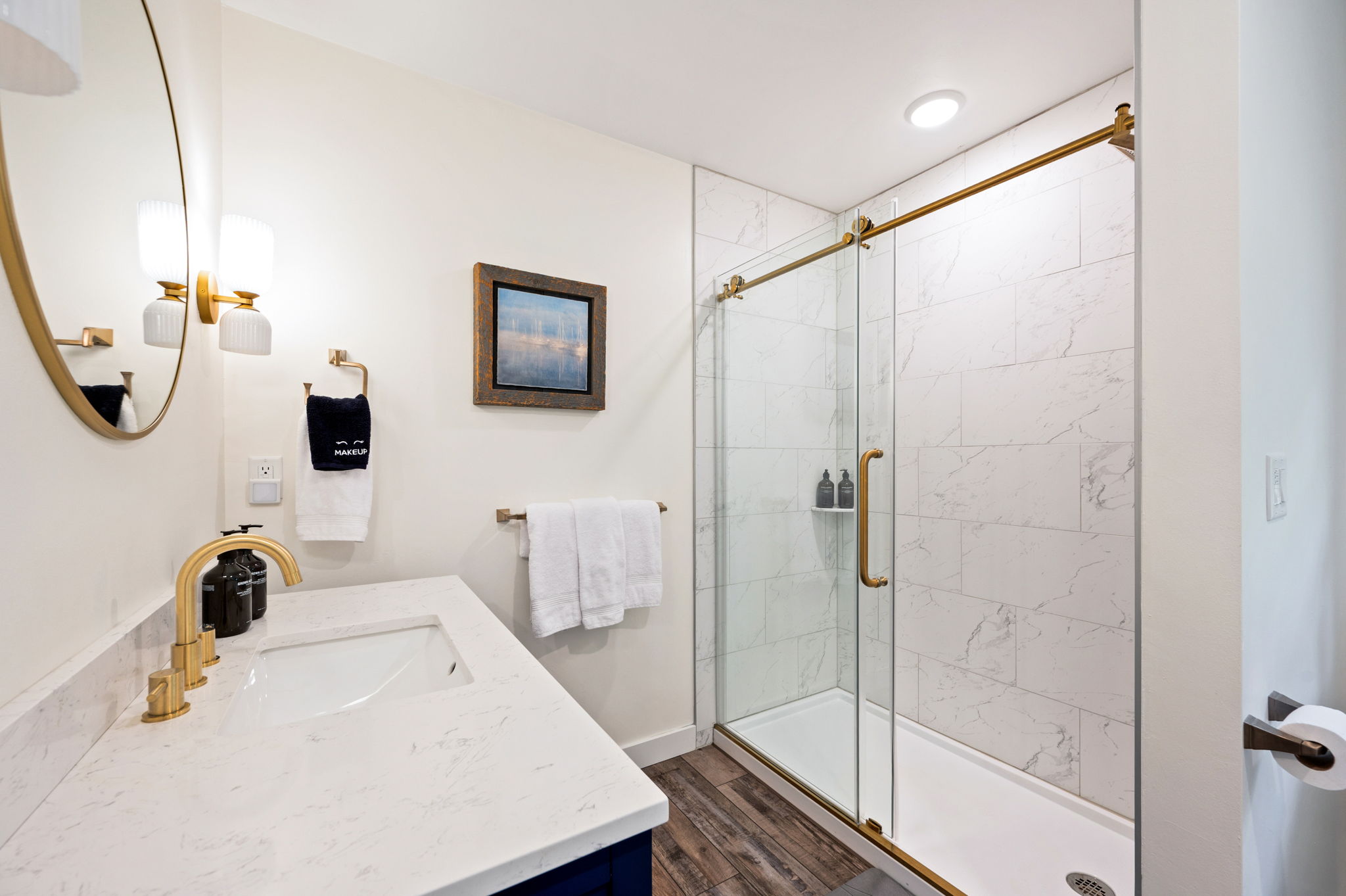 The second en suite bath dazzles with a navy vanity, warm gold fixtures, and a large walk-in glass shower wrapped in marble-look tile.