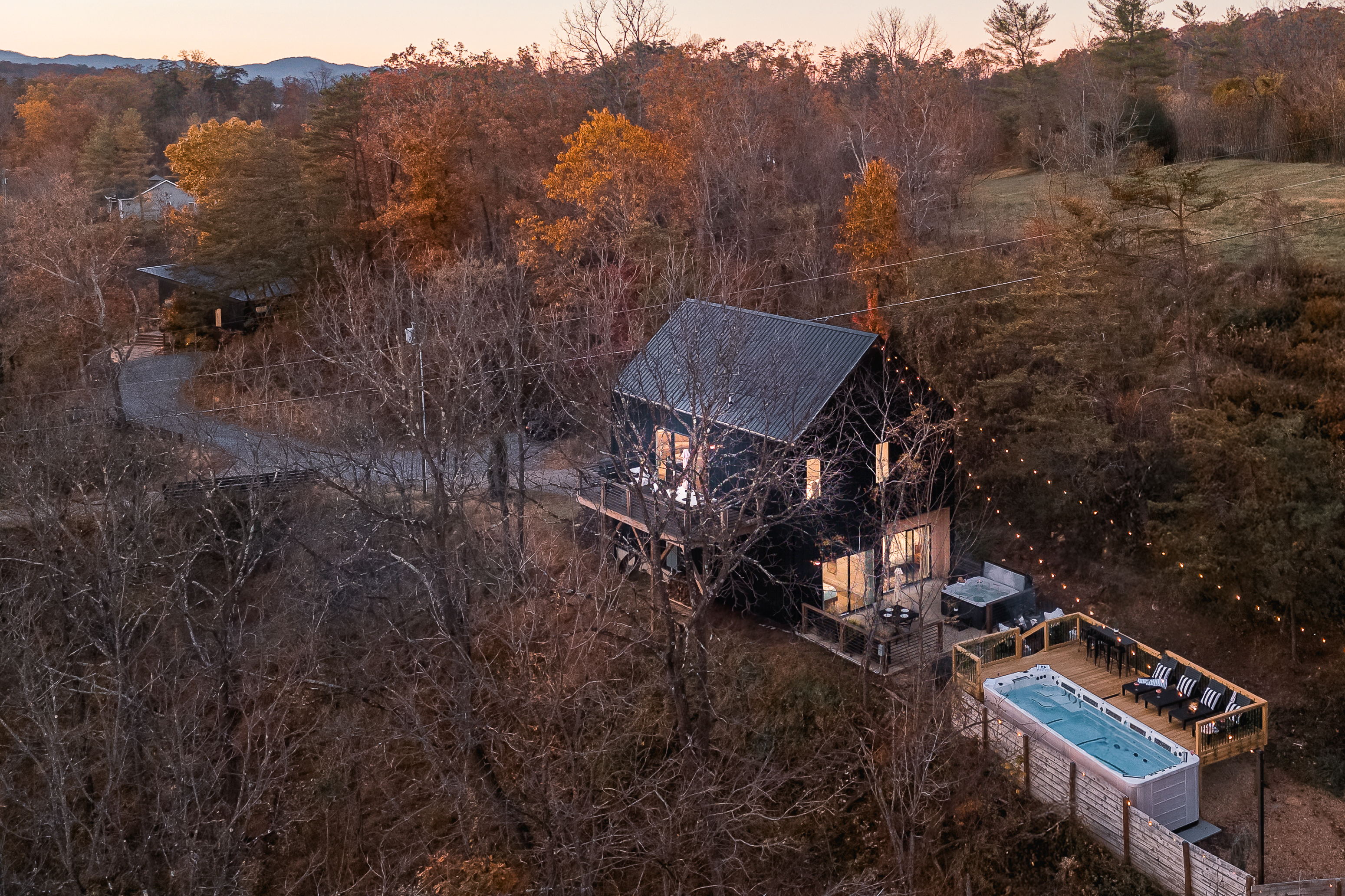 {Estate Aerial} Gallery House illuminates the hillside with warm string lights, with Glass House tucked just beyond—twin estates set amid rolling hills and Blue Ridge vistas, all moments from