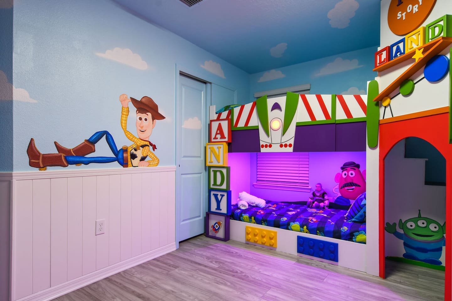 A whimsical Toy Story-themed bedroom with four twin beds, a private en suite bathroom with a shower, and a smart TV.