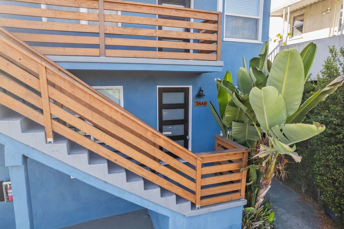 This home’s exterior features a stylish colorway, complemented by a beautifully designed staircase leading to a welcoming doorway. Lush greenery surrounds the entrance, adding natural charm to this inviting and elegant space.