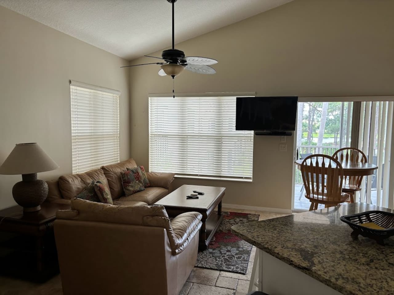 Comfortable living area with cozy seating, wall-mounted TV, ceiling fan, and natural light from the balcony doors.