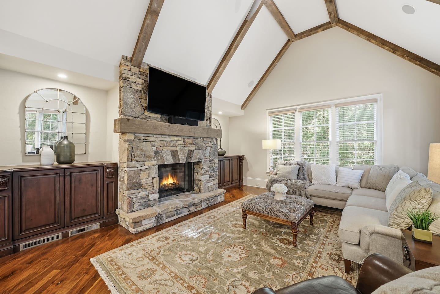 Relax in a warm and welcoming living room featuring high ceilings, a beautiful stone fireplace, and rich wood accents that create a cozy, home-like atmosphere. Enjoy a smart TV with a quality sound system perfect for movie nights and quiet mornings.