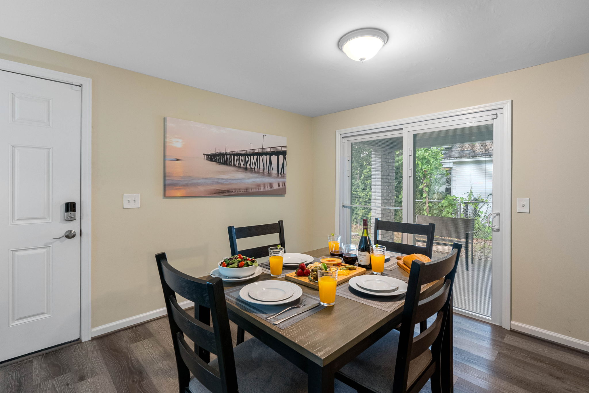 Positioned beside a glass door with vertical blinds, the dining area is filled with natural light during the day, creating an airy, uplifting ambiance.