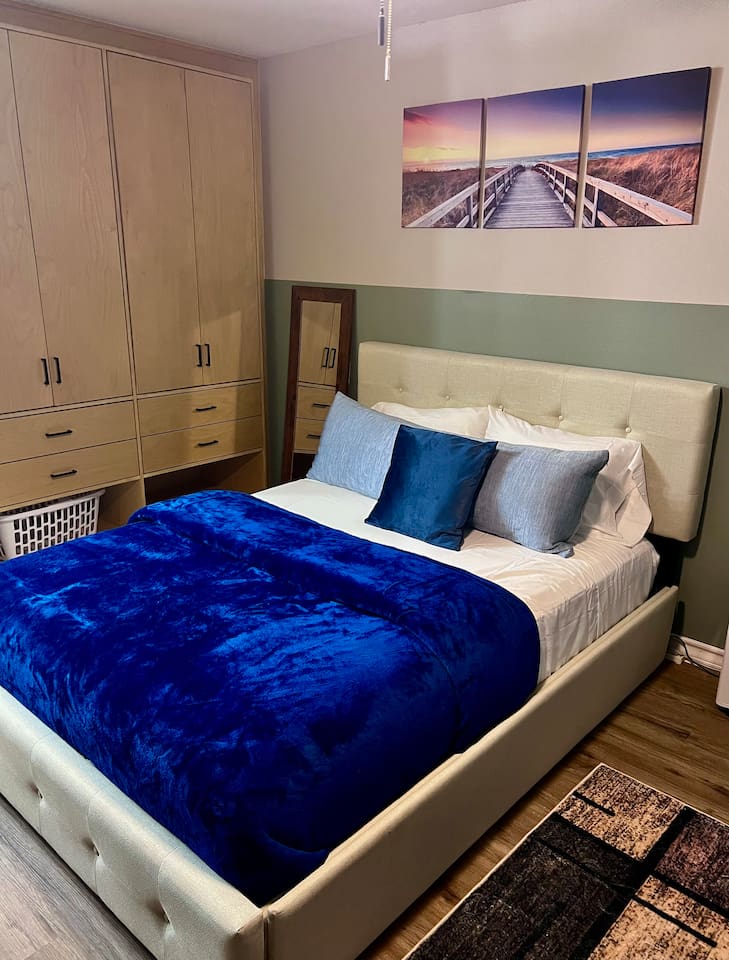 Queen bed with soft blue bedding and storage nearby for an easy stay.
