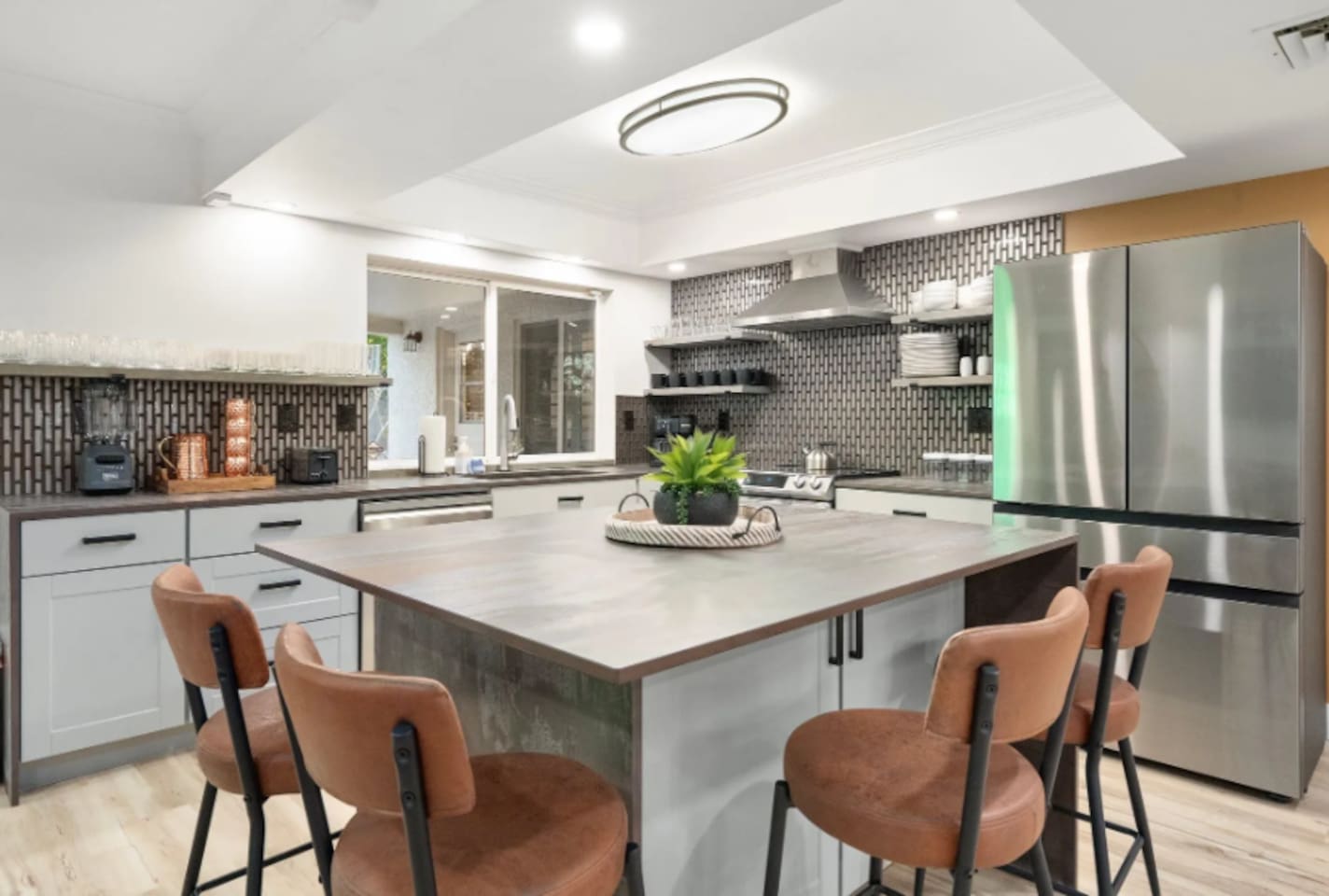 A spacious island with leather stools invites everyone to gather while the cook works their magic, with sleek stainless appliances rounding out the space.
