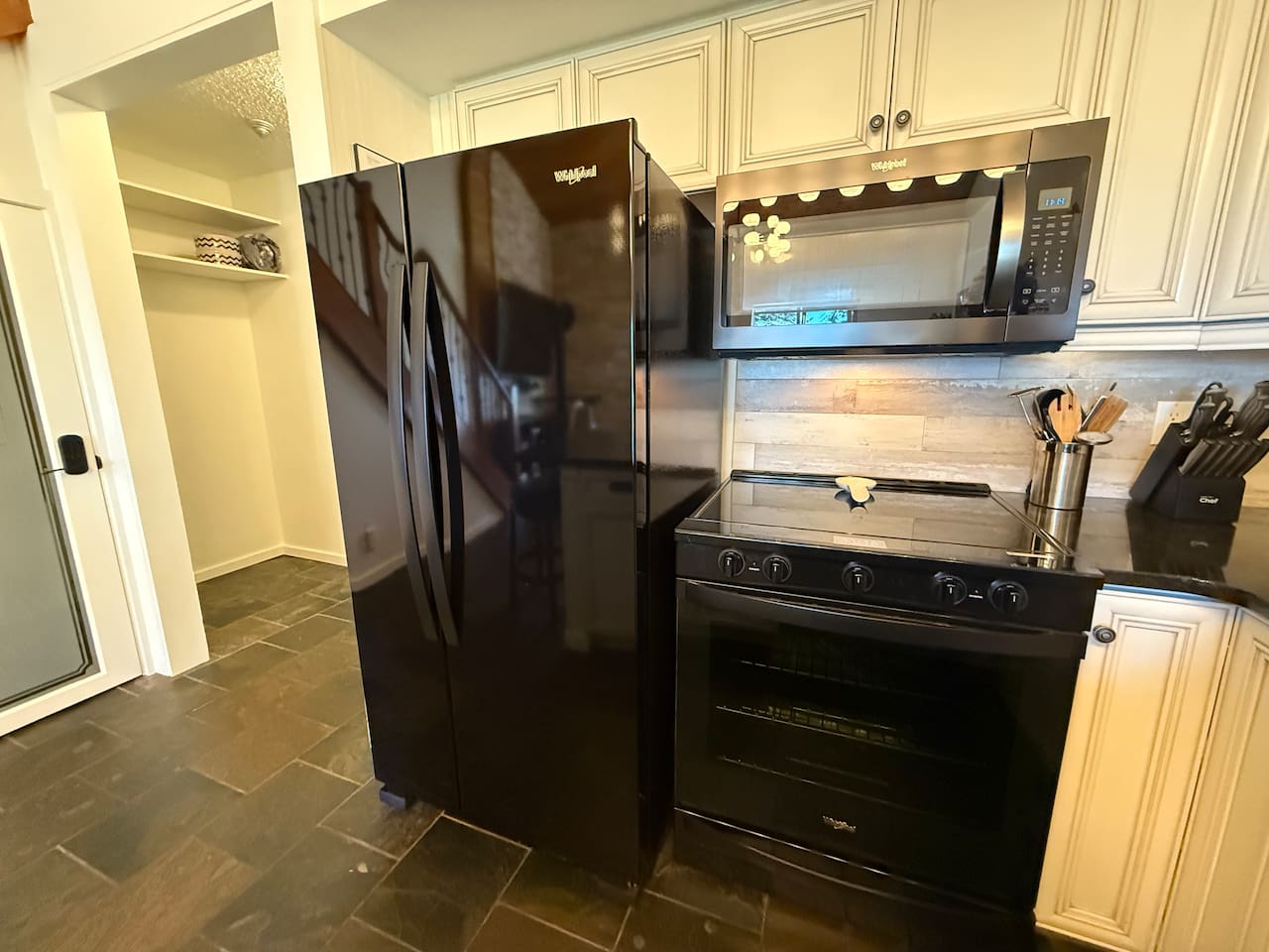Full-Size Appliances: A stylish black side-by-side refrigerator and glass top stove complement the modern kitchen design and stone flooring.