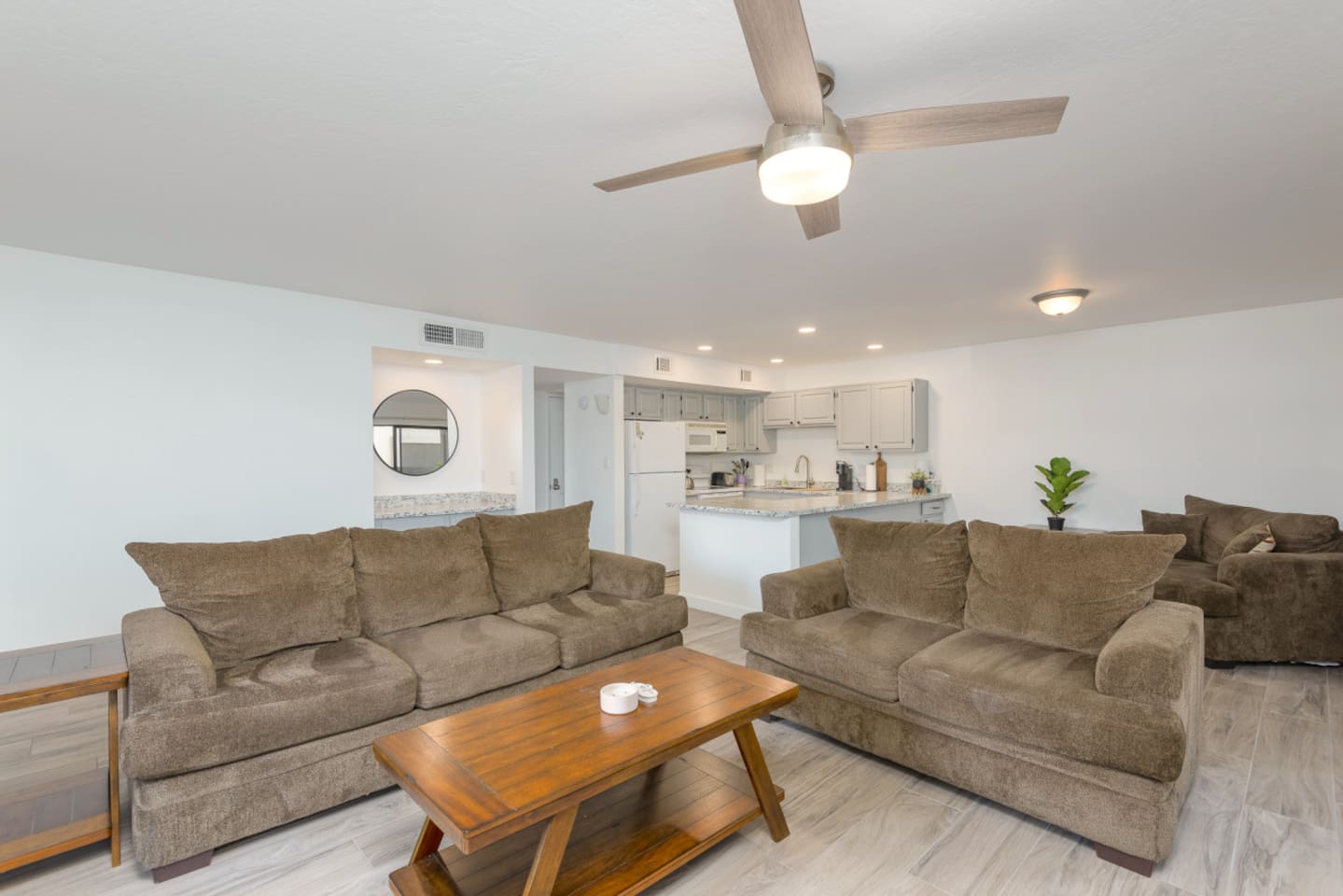 Living room with comfortable seating, a fireplace, ceiling fan, and an open view into the kitchen.
