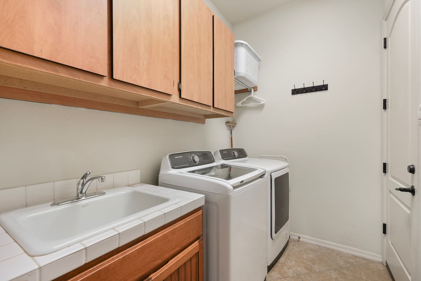 Laundry area with full-size washer and dryer, utility sink, overhead storage cabinets, and wall hooks for added convenience.