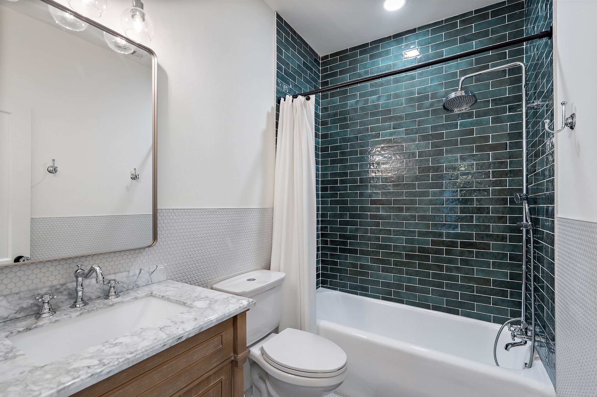 Bathroom 2 rain shower/tub combo with deep green subway tile surround, marble vanity, and updated fixtures. Stocked with Ginger Lily Farms shampoo, conditioner, and shower gel. Fresh towels and hairdryer provided.