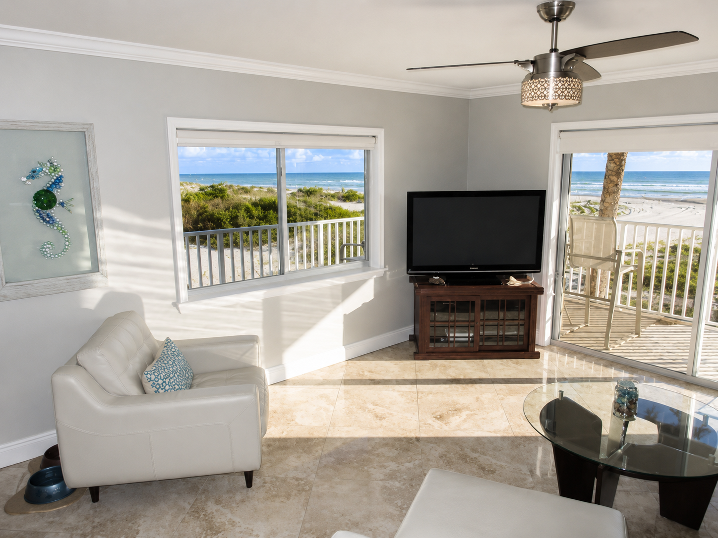 Bright living room with ocean view, white armchair, and balcony overlooking beach.