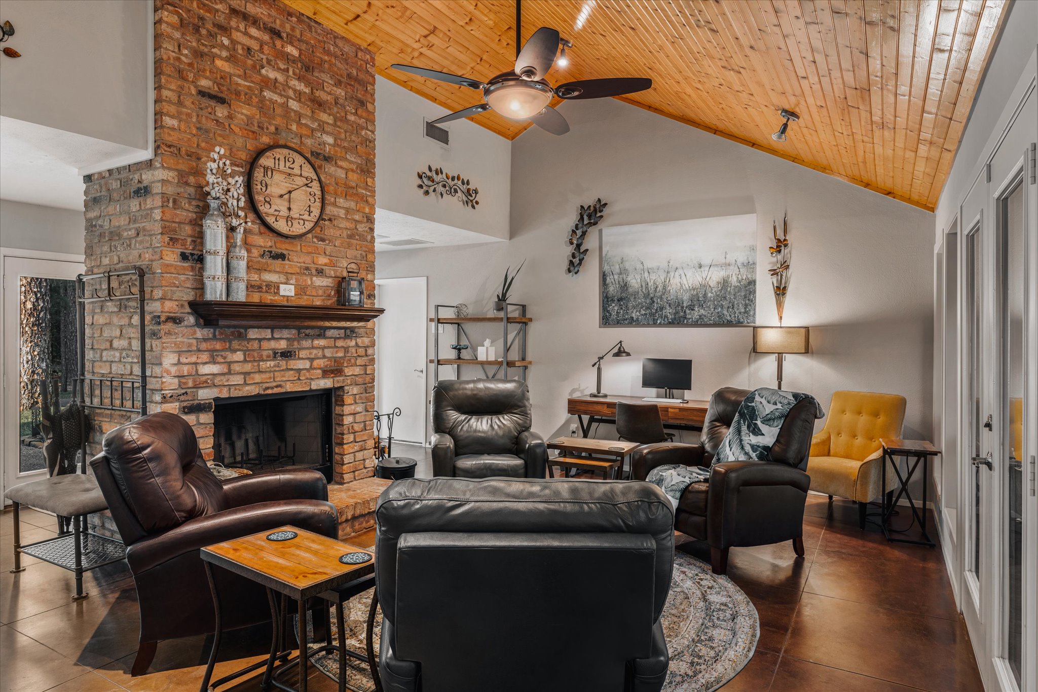 A cozy and inviting living space featuring a stunning brick fireplace, vaulted wood ceiling, and stylish seating. Perfect for relaxing, gathering, and enjoying the warmth of this beautifully d