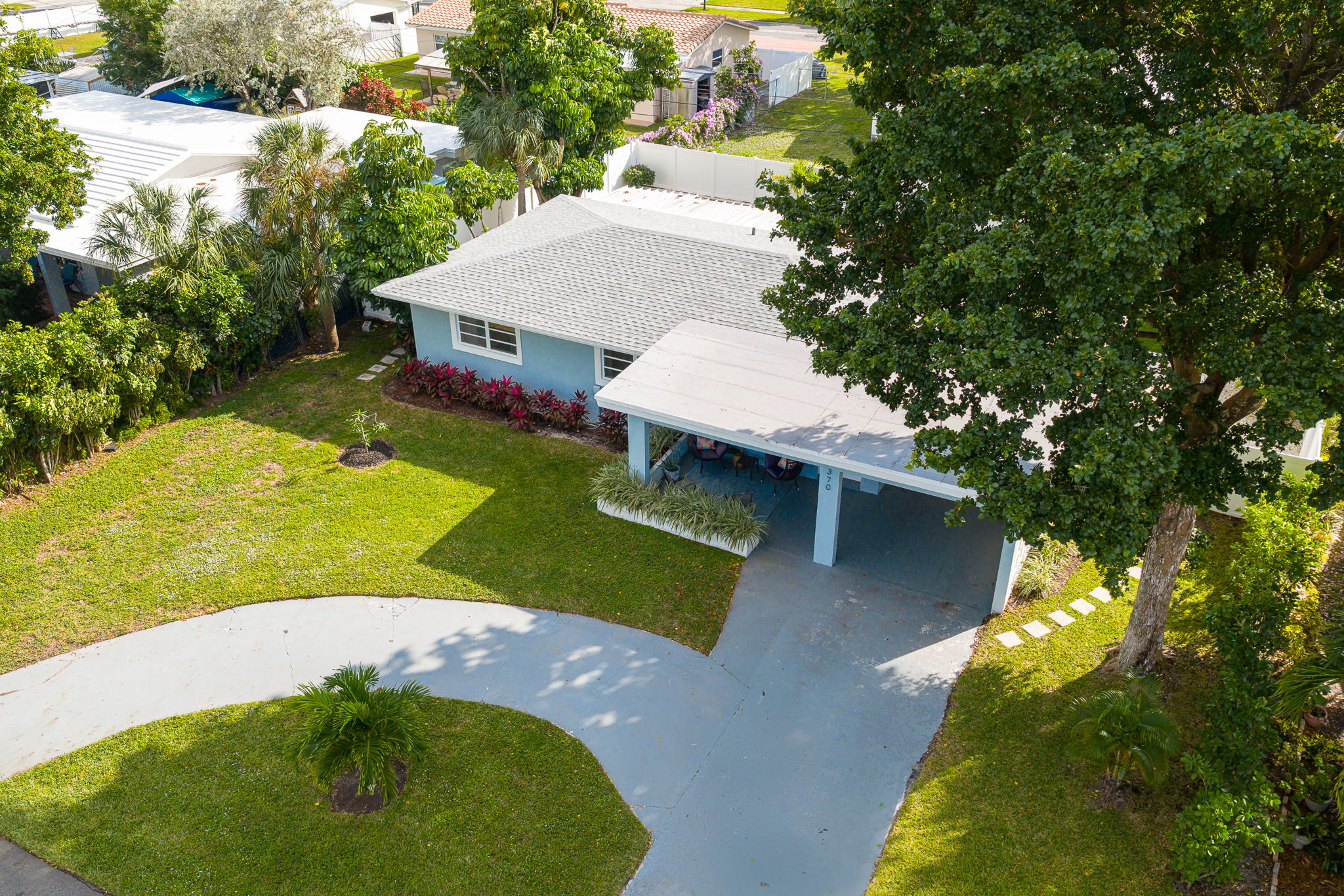 Soaring aerial perspectives highlight the home’s tranquil Pompano Beach neighborhood, private backyard oasis, covered carport, and extended driveway with space for 3 cars.