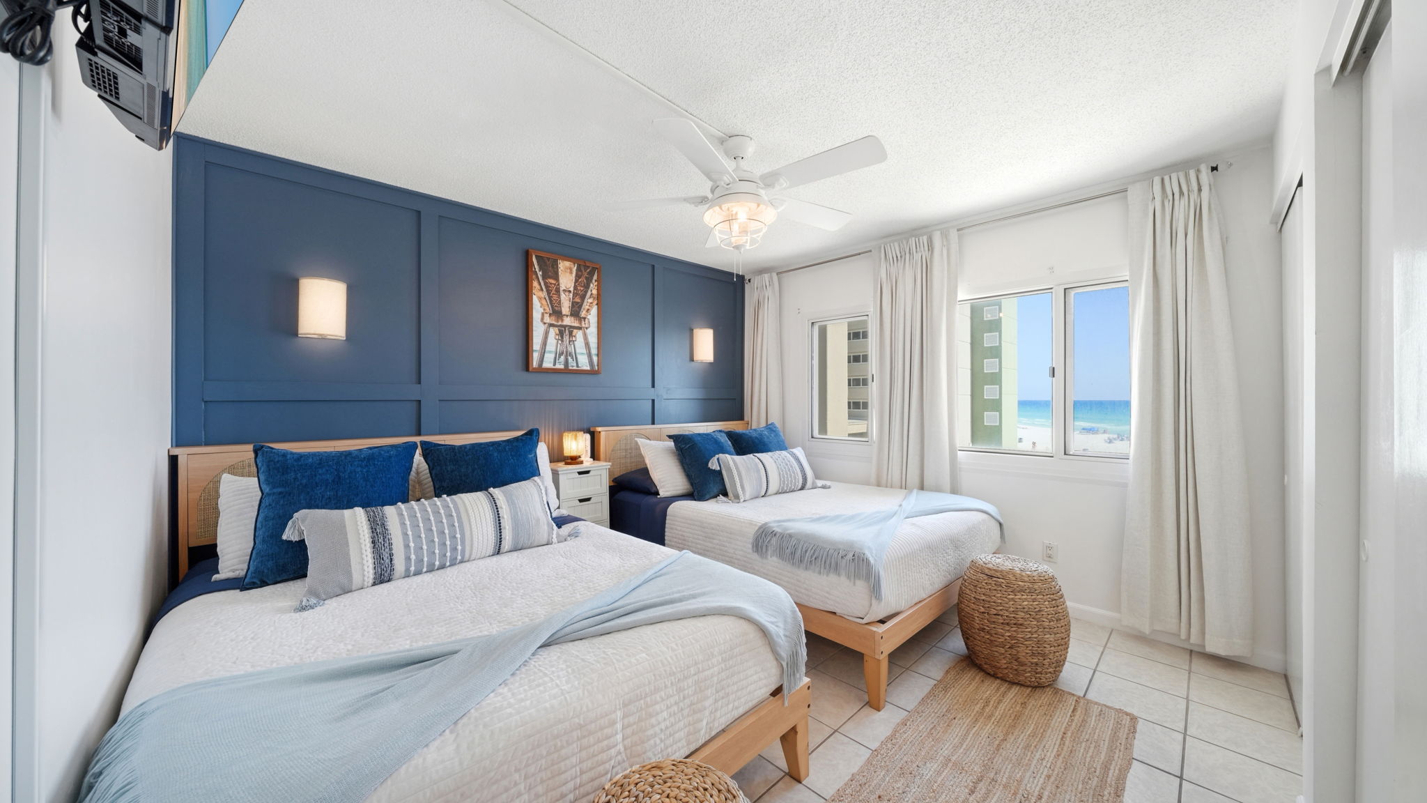This professionally designed bedroom features 2 queen beds, storage baskets for throw pillows and blankets, cordless sconces, blackout curtains, luxury bedding and stunning beach view from the panoramic window