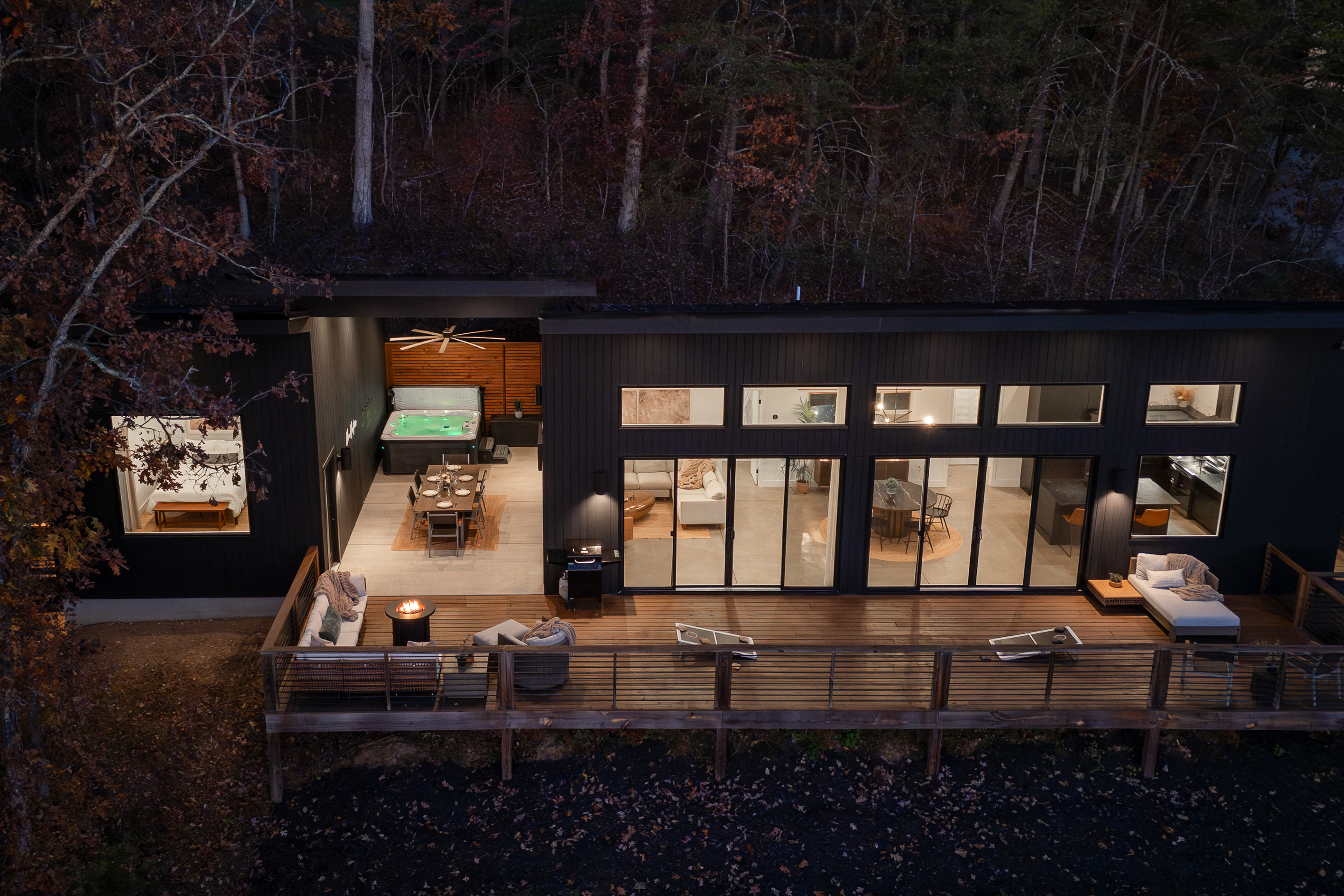 {The Iconic Glass House} Evenings flow effortlessly here—hot tub bubbling, dinner around the long table, fire-pit conversations, and a round of cornhole as the forest settles into night.