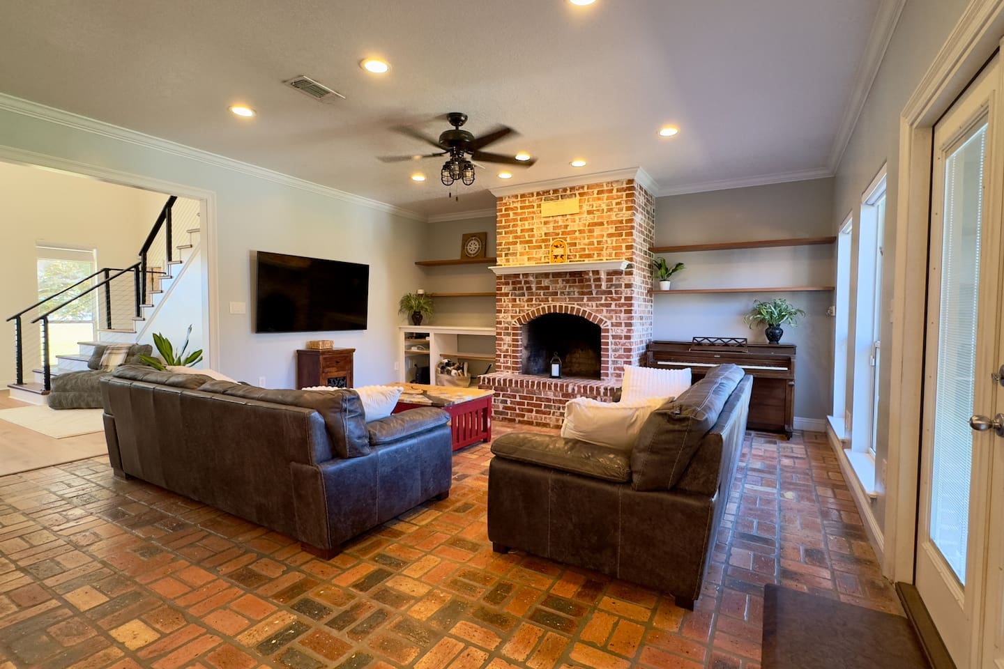 A flat-screen TV, piano, and decorative shelving with plants and a clock create a lively, inviting atmosphere.

