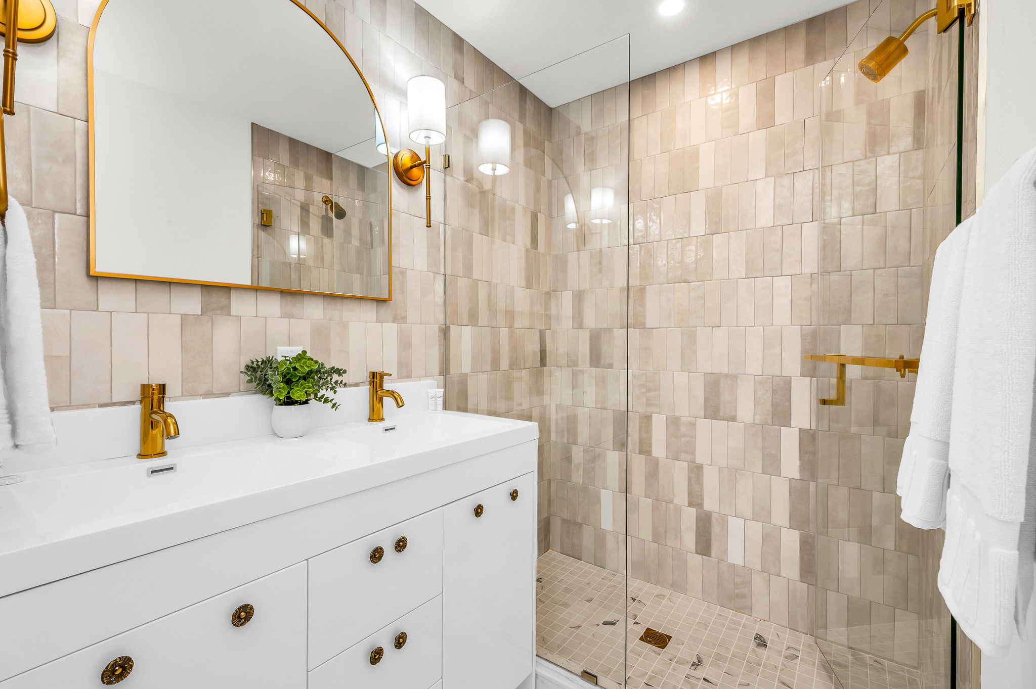 Spa-inspired primary ensuite—this fully renovated designer bathroom showcases a stunning walk-in shower with handcrafted tile, a dual vanity with gold fixtures, and elevated finishes throughout for a truly luxurious retreat.