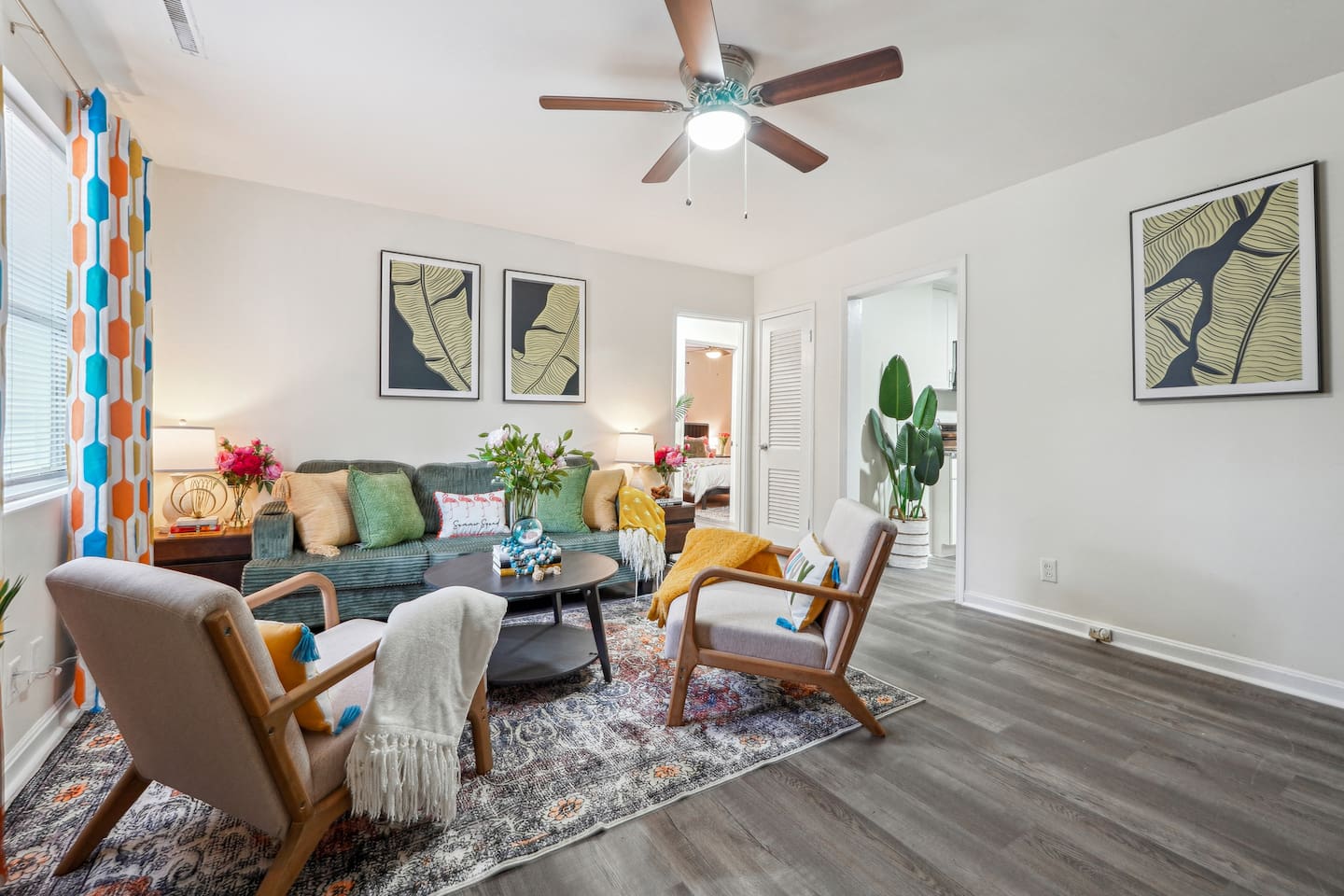 Enjoy a cozy living room featuring a long comfortable sofa, a TV for your entertainment, a ceiling fan, two chair, and a window with a lovely view outside — perfect for relaxing and unwinding.
