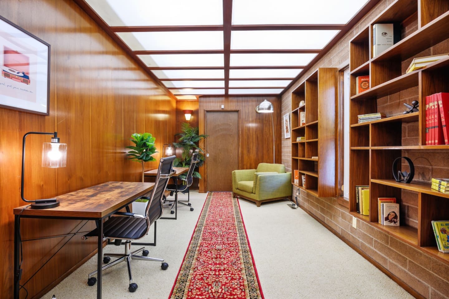 Library with two desks, two lounge chairs, and a collection of books from the era the house was built.