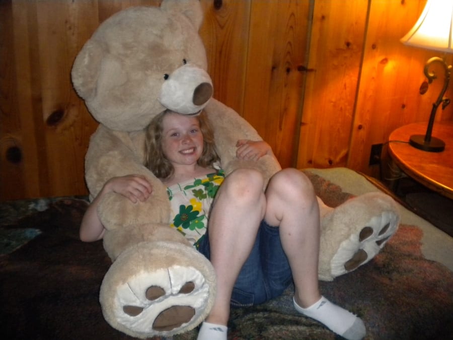 Child smiling with a giant teddy bear in a cozy wood-paneled room at the lodge