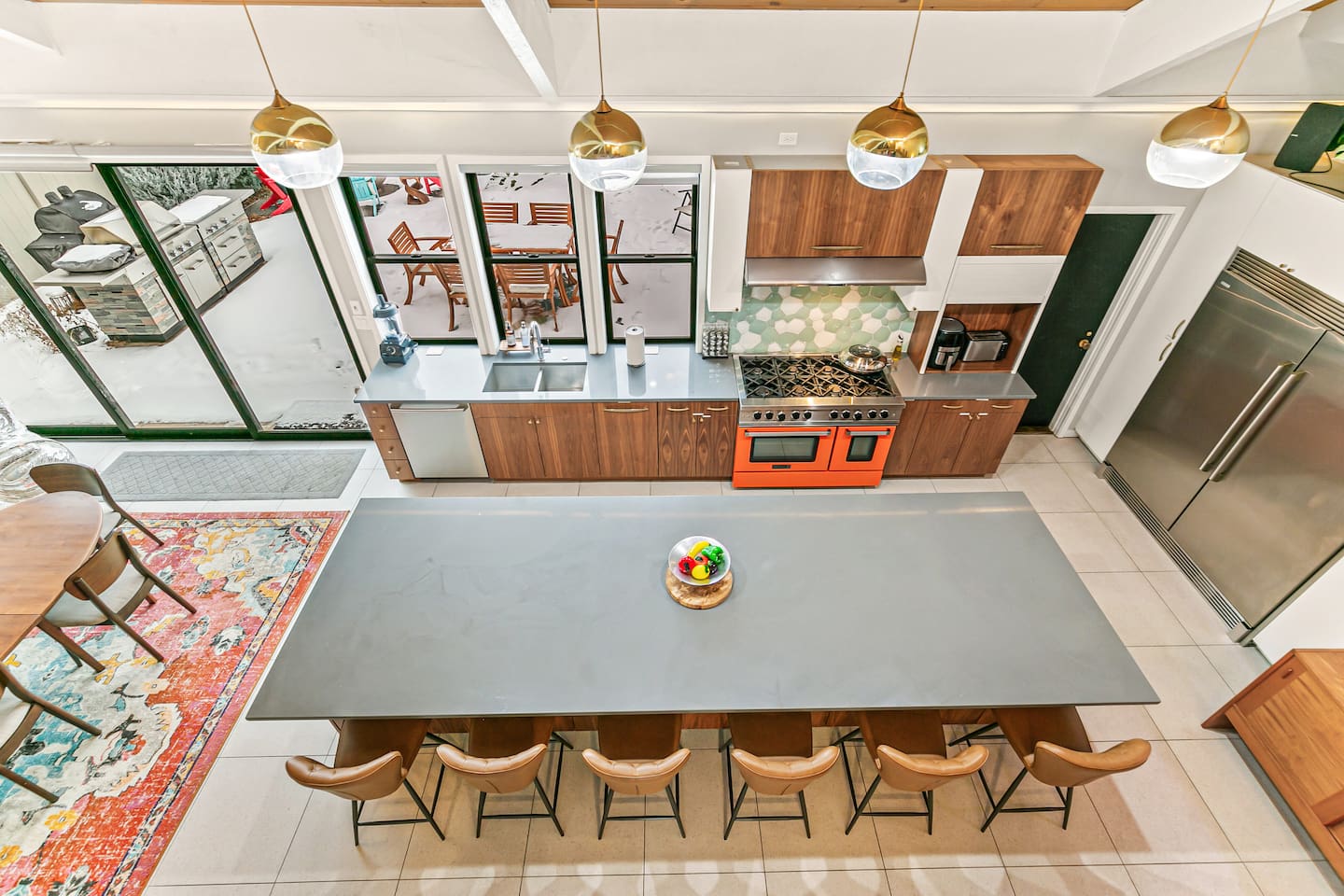 The kitchen is fully equipped with modern appliances, a Mid-Century Modern interior design, a large fridge, freezer, and ample storage. It boasts a spacious layout and a 16 ft island table, with convenient access to the outdoor area.
