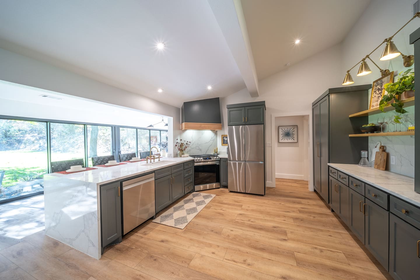 Open-concept kitchen with a large marble island, breakfast bar seating, stainless steel appliances, and a gas range. Custom cabinetry, warm brass fixtures, and abundant natural light make this space ideal for cooking, gathering, and casual dining.