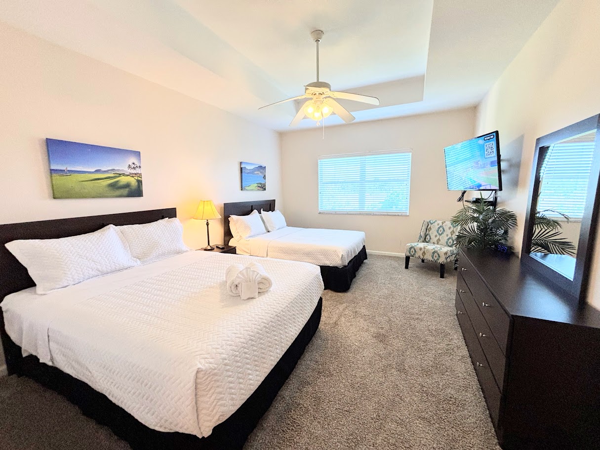 Comfortable bedroom with two beds, ceiling fan, TV, dresser storage, and natural light.