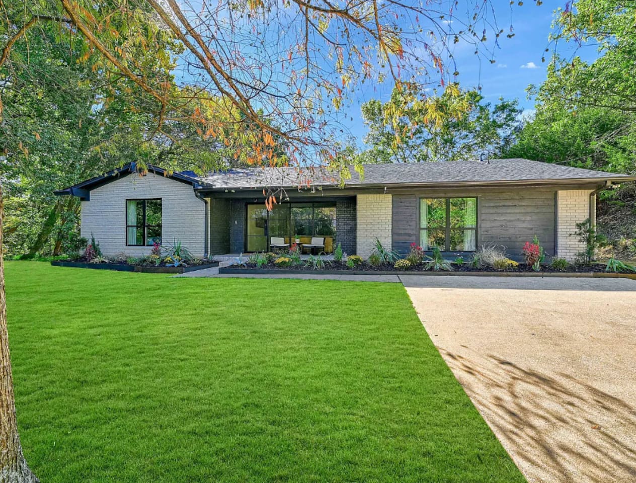 Front exterior view showcasing the modern ranch-style home, landscaped yard, and welcoming curb appeal surrounded by mature trees.