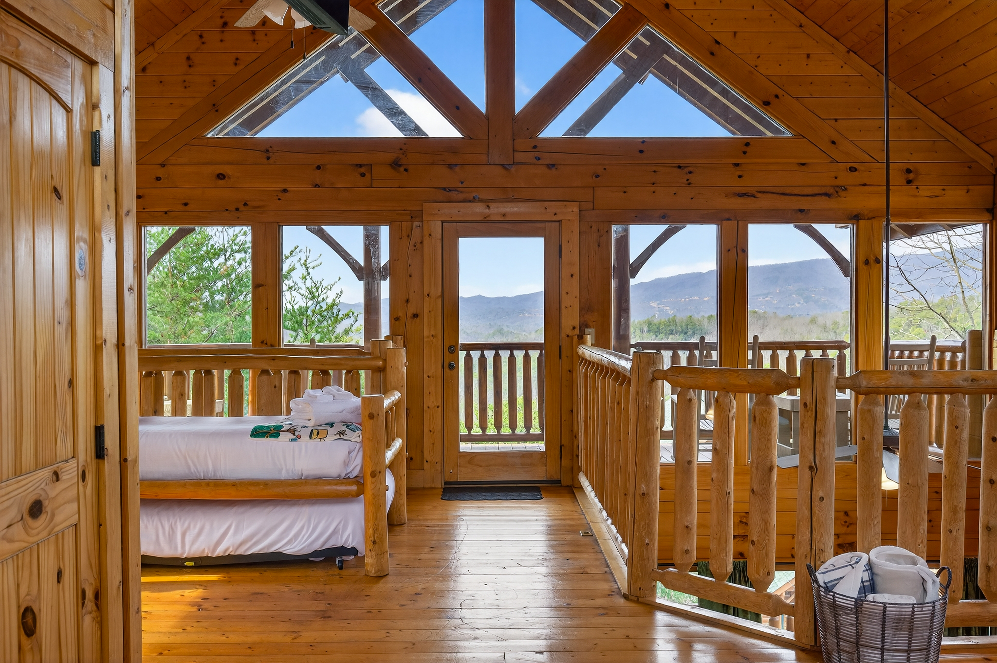 Upper level king suite — soaring A-frame skylights, wraparound Smoky Mountain views, private deck access, Smart TV, and a trundle that sleeps two more right in the room.