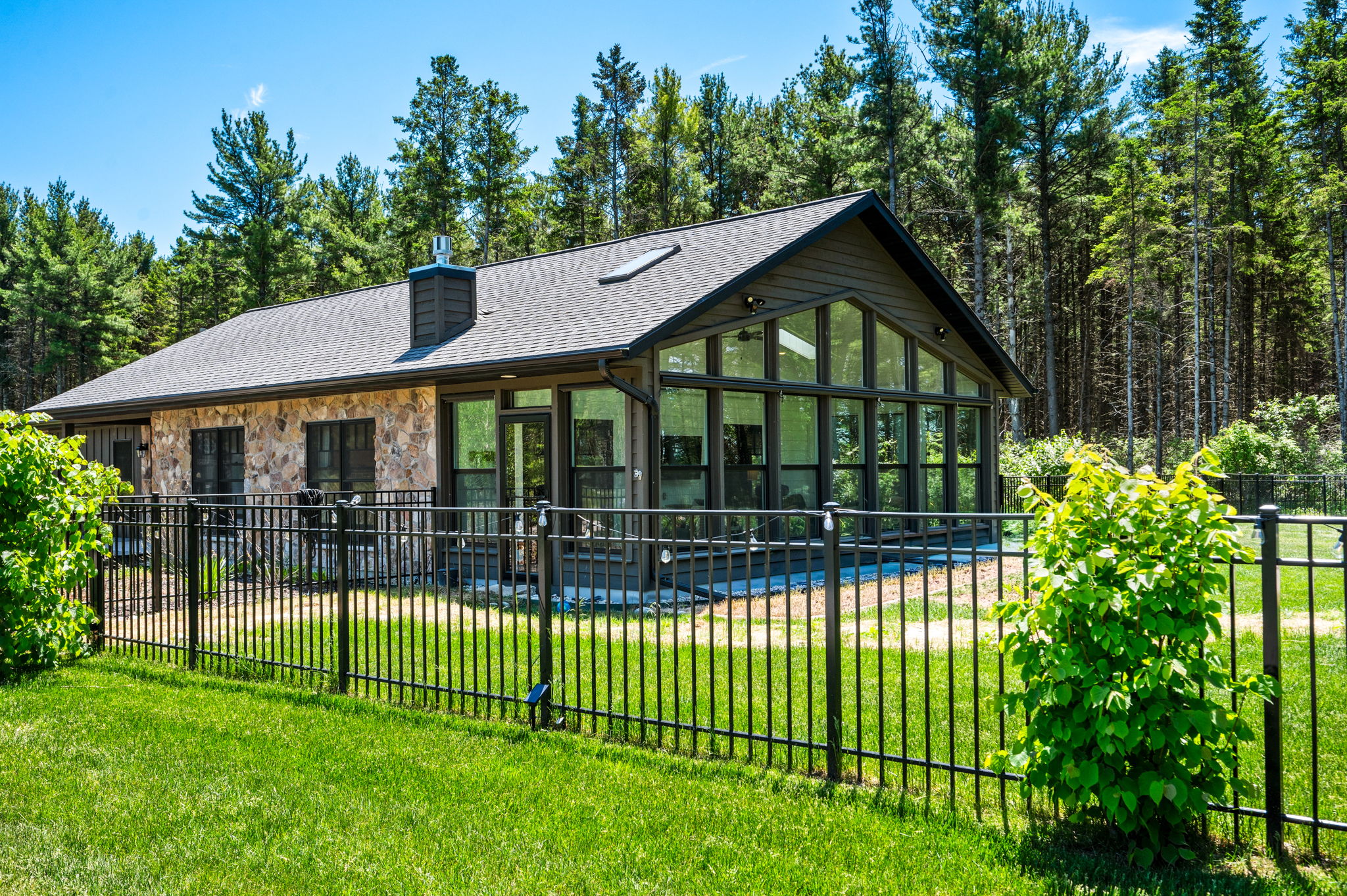 Enjoy your time in this modern Northwoods retreat, where a soaring glass-gabled sunroom and natural stone accents are wrapped by a private, fenced yard tucked into towering pines.