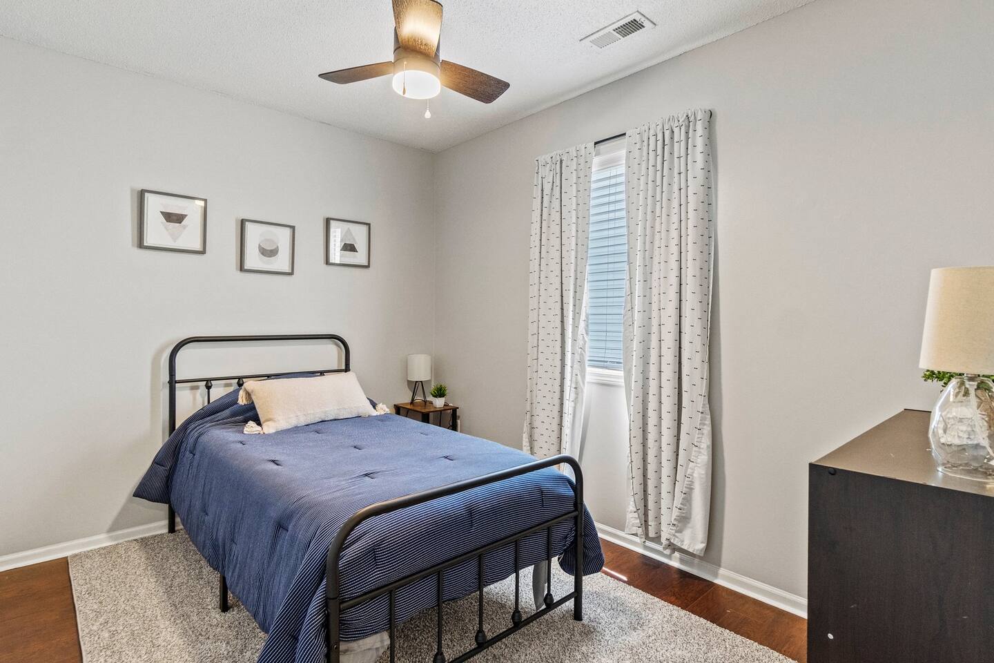 This inviting bedroom features a single bed with deep navy bedding, a minimalist black metal frame, and neutral walls for a calm and restful vibe.