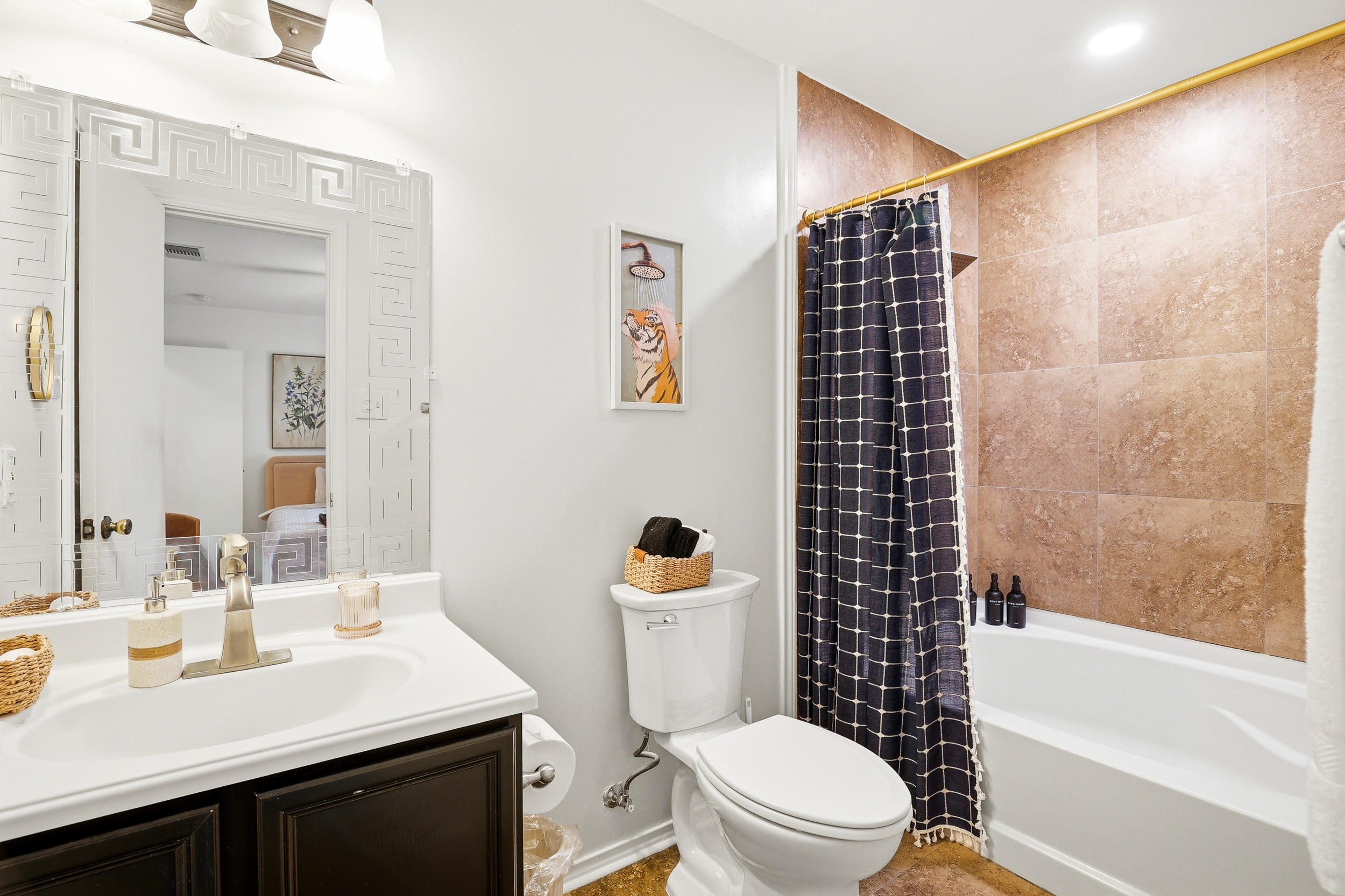 Shower and tub combo with gold curtain rod, patterned curtain, and rain-style showerhead. Clean, well-maintained, and stocked with toiletries for a comfortable start to every morning.