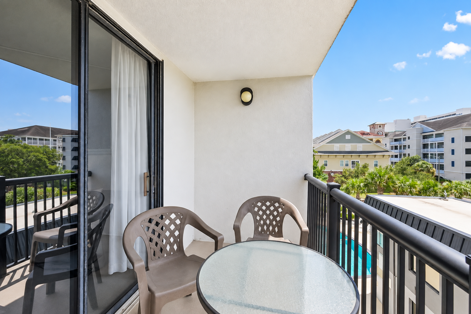 Covered balcony with table seating, chairs, and a treetop view over the Holiday Towers area.