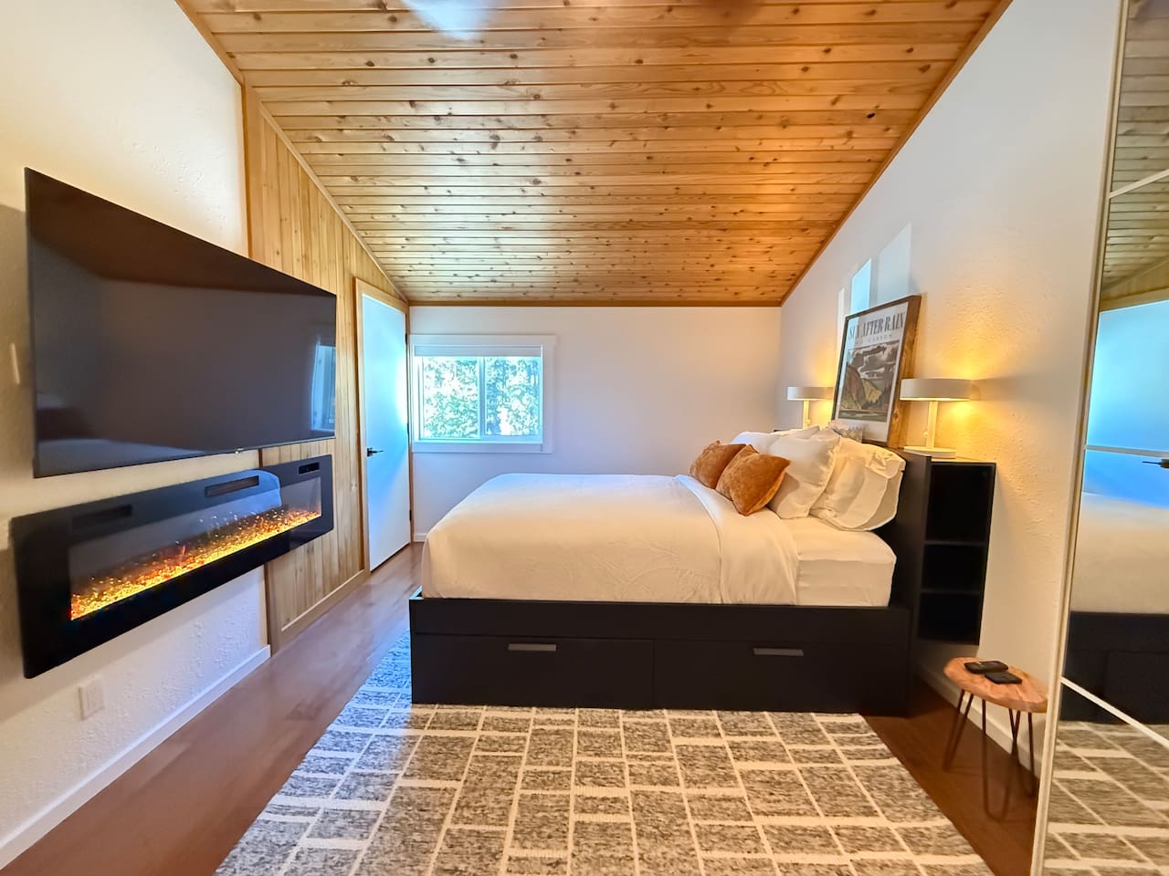 Primary Loft Bedroom: A spacious loft bedroom featuring a comfortable queen-size bed, a modern built-in electric fireplace, a 65" Smart TV, closet with mirrored doors and integrated under-bed storage solutions for your gear.