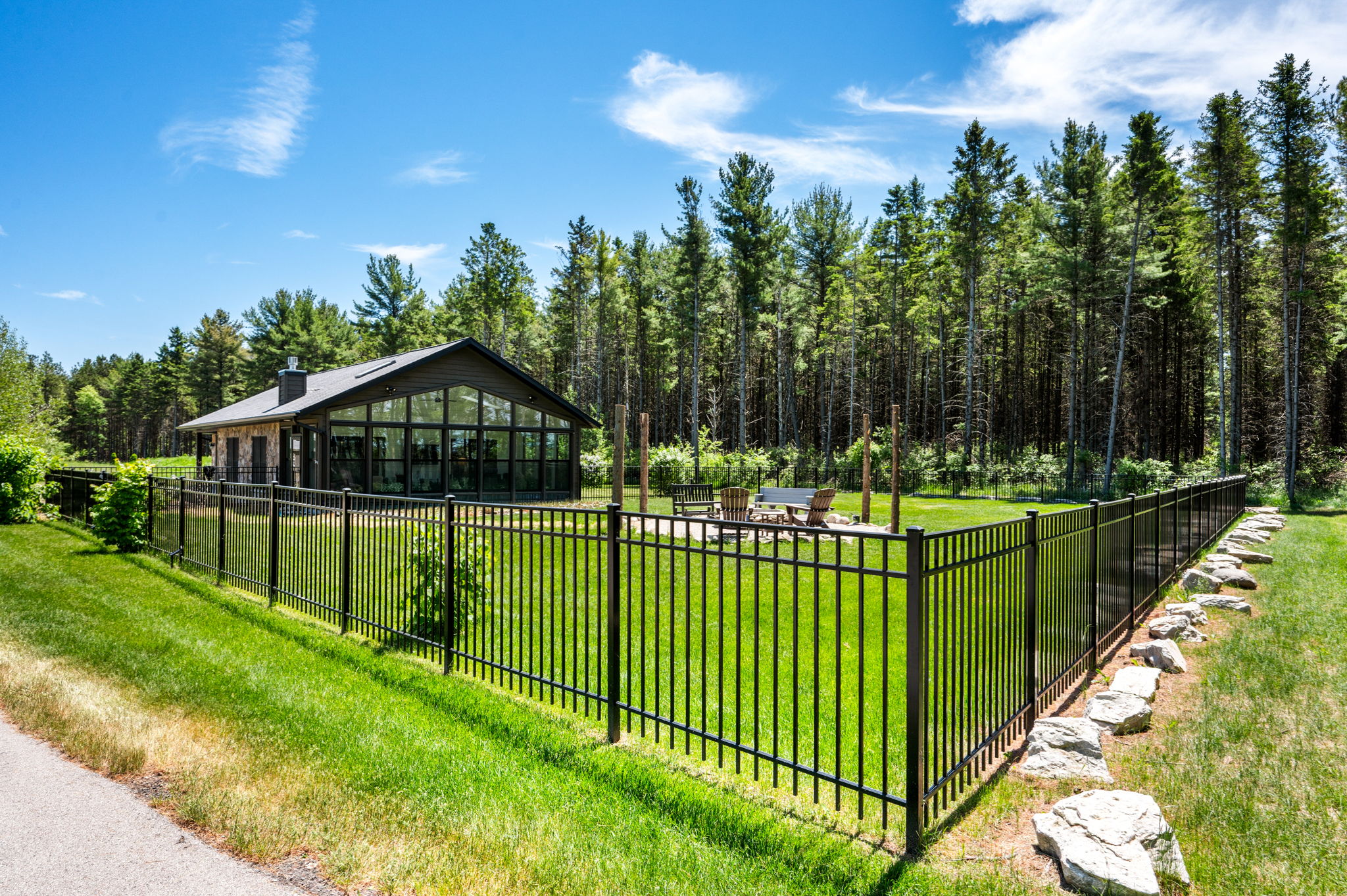 Gather around the backyard fire pit with cozy Adirondack chairs and benches, all set against a wall of windows and a serene forest backdrop.