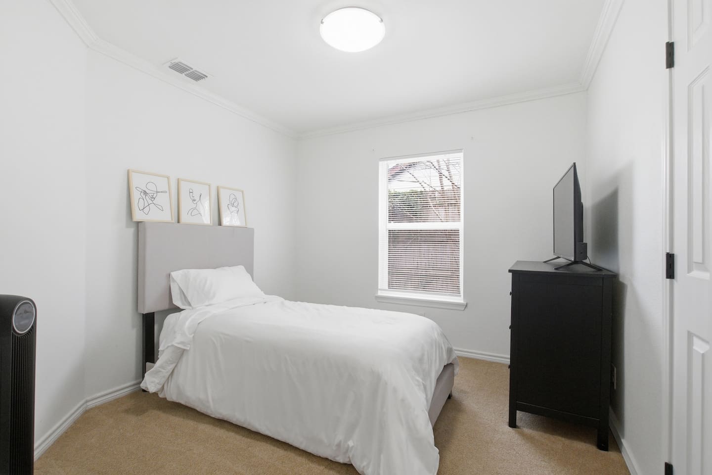 Bright guest bedroom featuring a twin bed, soft bedding, Smart TV, and room darkening shades for privacy and sleep.