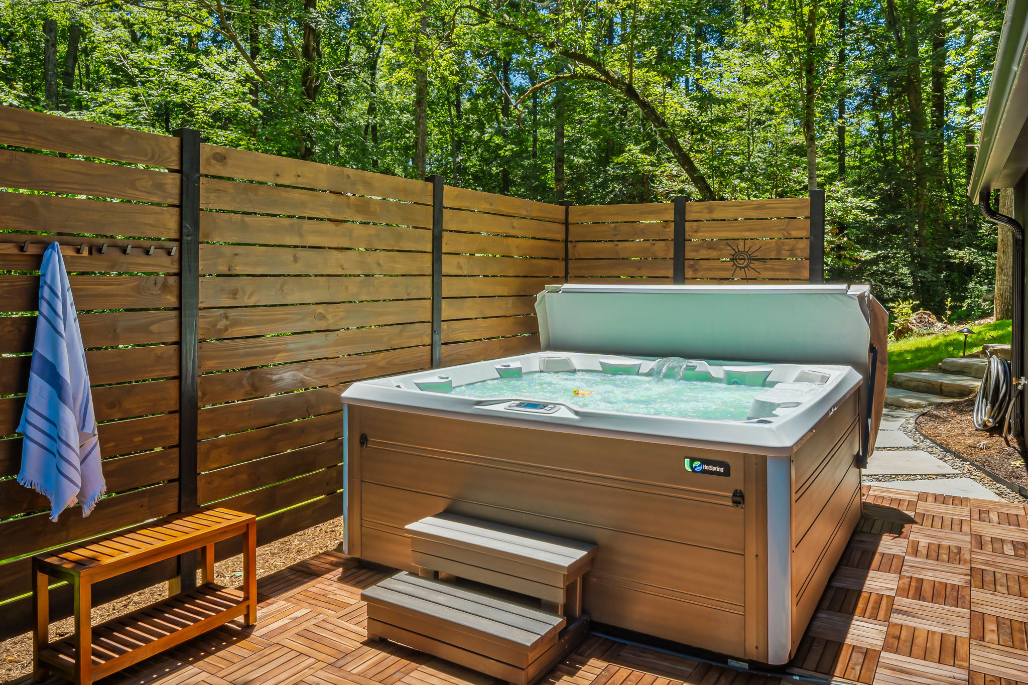 A winding stone walkway lit by landscape lights leads to a private hot tub patio surrounded by trees.The spacious hot tub seats up to 7 adults, perfect for unwinding after a day of adventure or stargazing under the night sky.