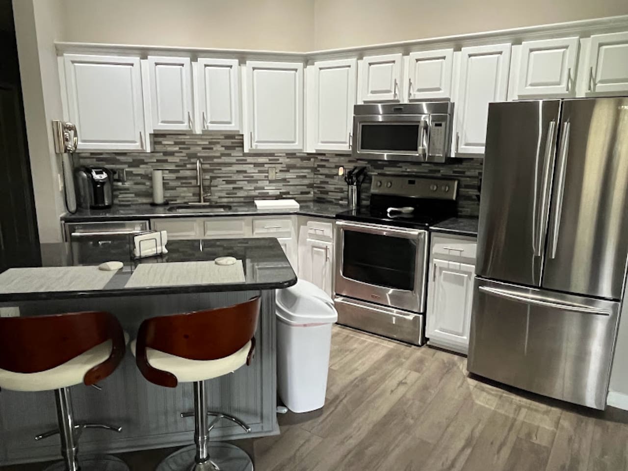 Updated kitchen featuring stainless steel appliances, white cabinetry, tile backsplash, breakfast bar seating, and wood-look flooring.