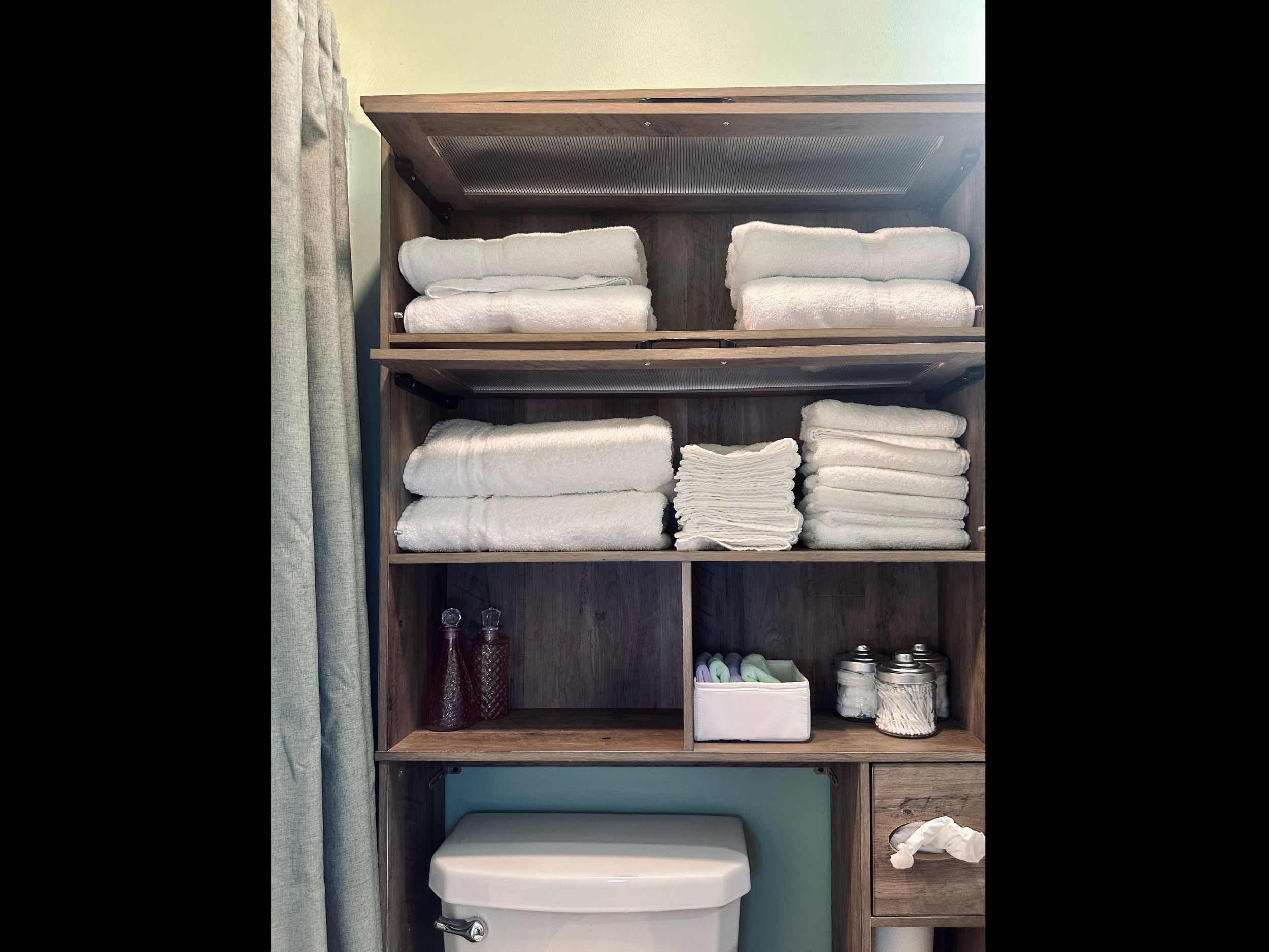 Hall bathroom storage featuring fresh bath towels, hand towels, washcloths, makeup remover cloths, and organized containers with cotton balls and swabs.