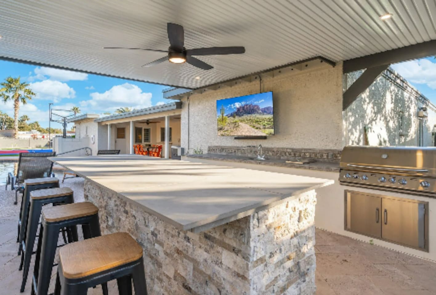 Bar stools line the outdoor kitchen, with a mounted TV keeping the group entertained while the grill does its work.
