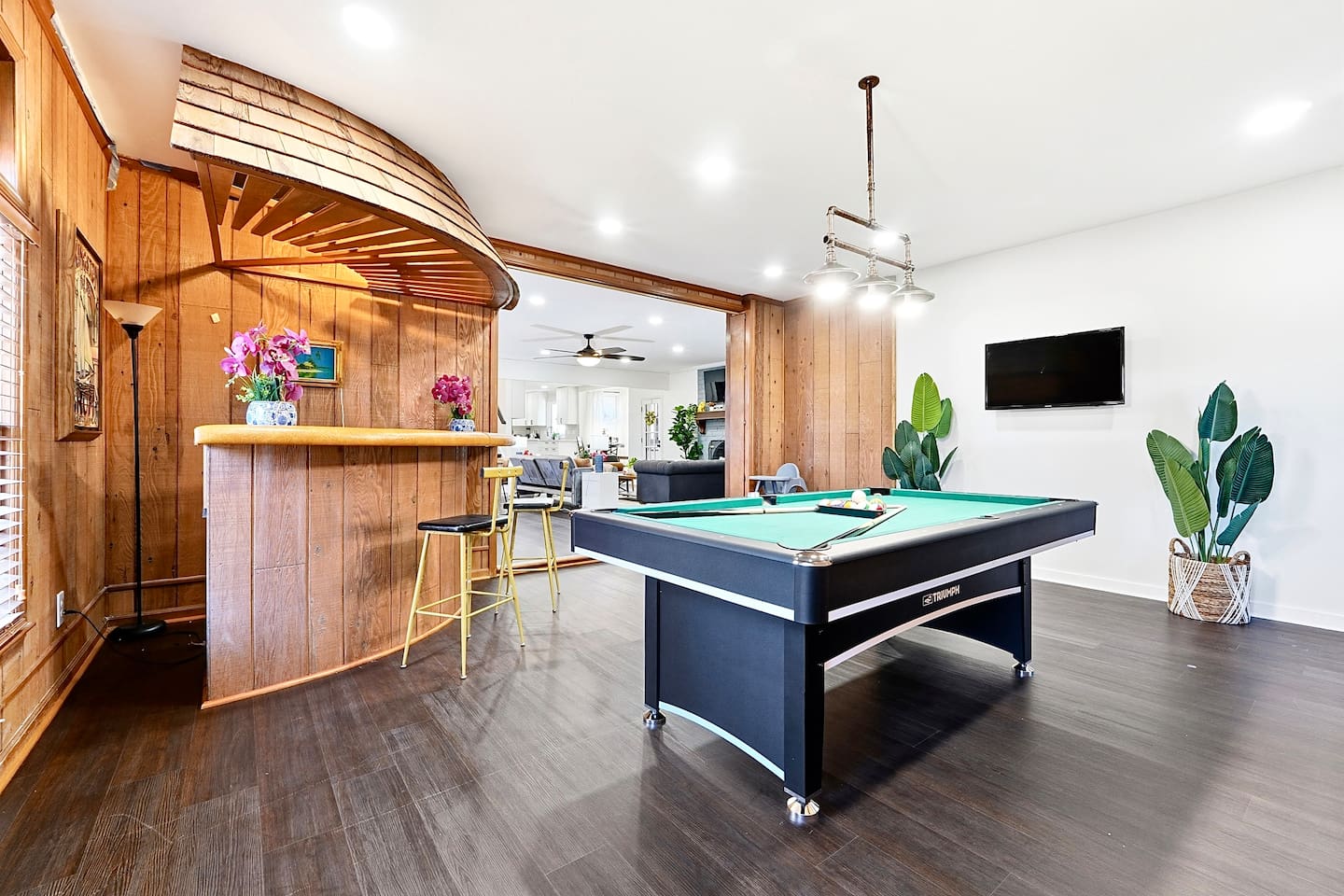 Enjoy this main-floor game room near the side entrance featuring a convertible pool and ping-pong table, a custom curved wood bar, and a Roku powered smart TV—ideal for entertaining and casual gatherings.