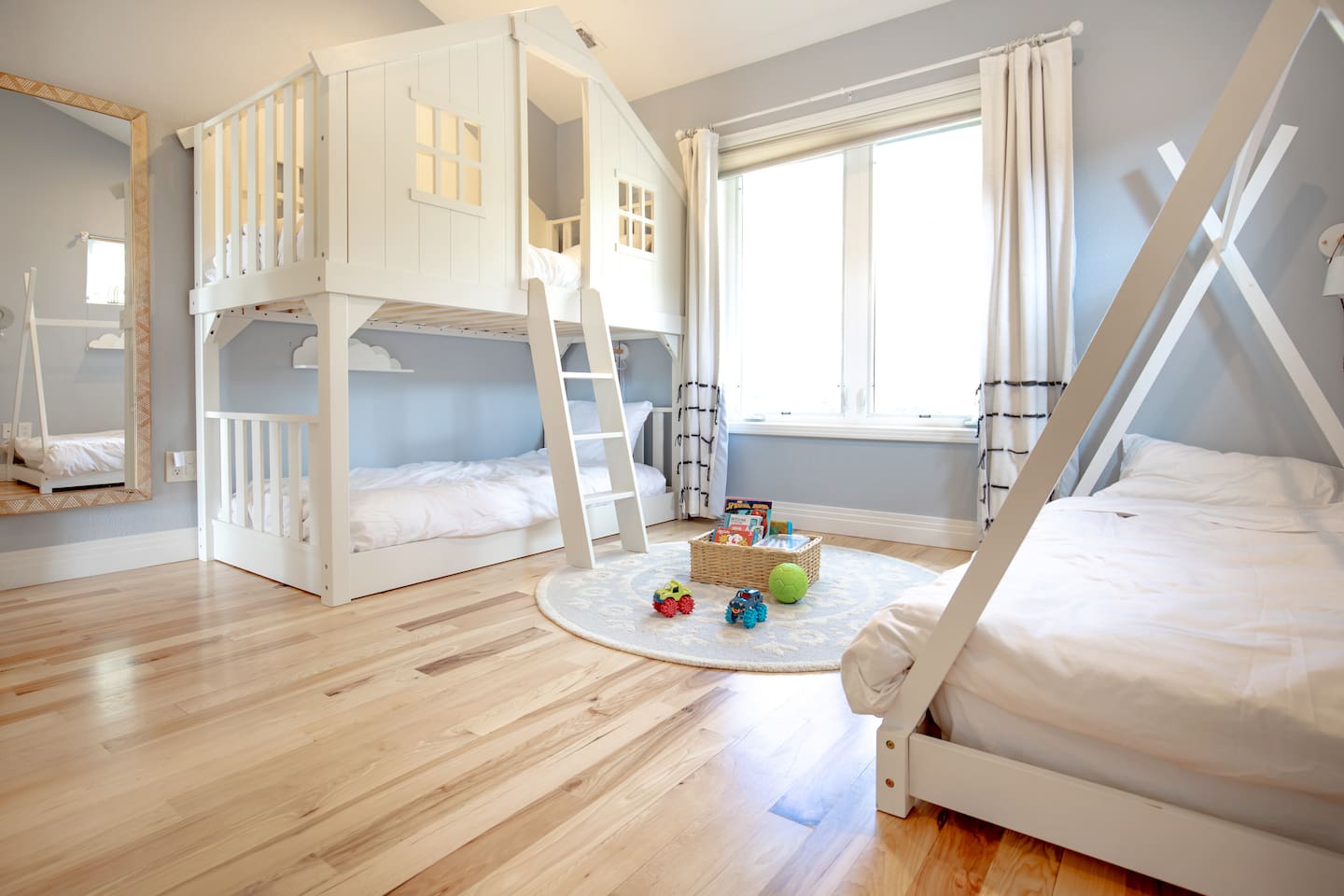 A cheerful and spacious kids’ room with a charming house-style bunk bed, a single tent bed, and plenty of natural light—perfect for little adventurers