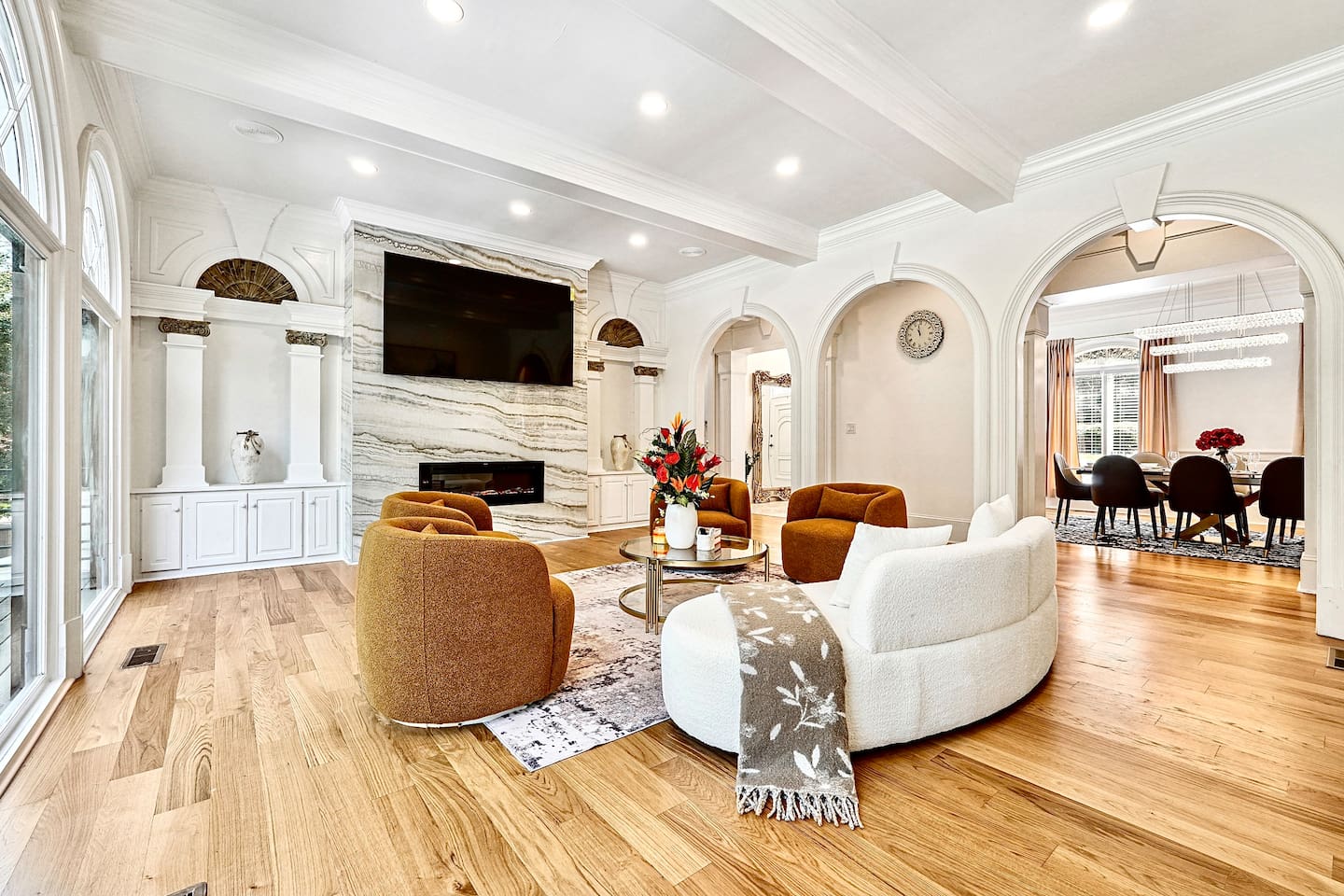 Located straight ahead from the front entry, this main-floor living room showcases a striking modern design with a round shaped contemporary sofa, four orange accent chairs, a smart TV, and a fireplace for a warm, elevated lounge experience.