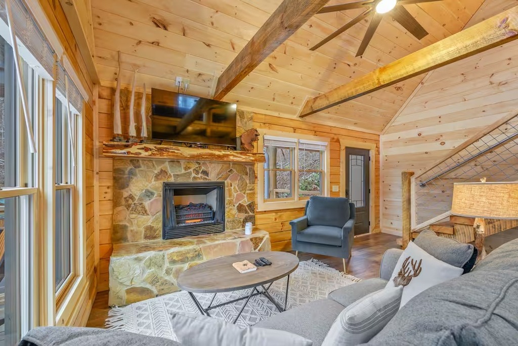 The main living area of Bear Paws Cabin was designed for families who want to be together. Soaring vaulted ceilings with exposed timber beams, an open-concept layout connecting the living room and kitchen, and large windows looking out into the wilderness
