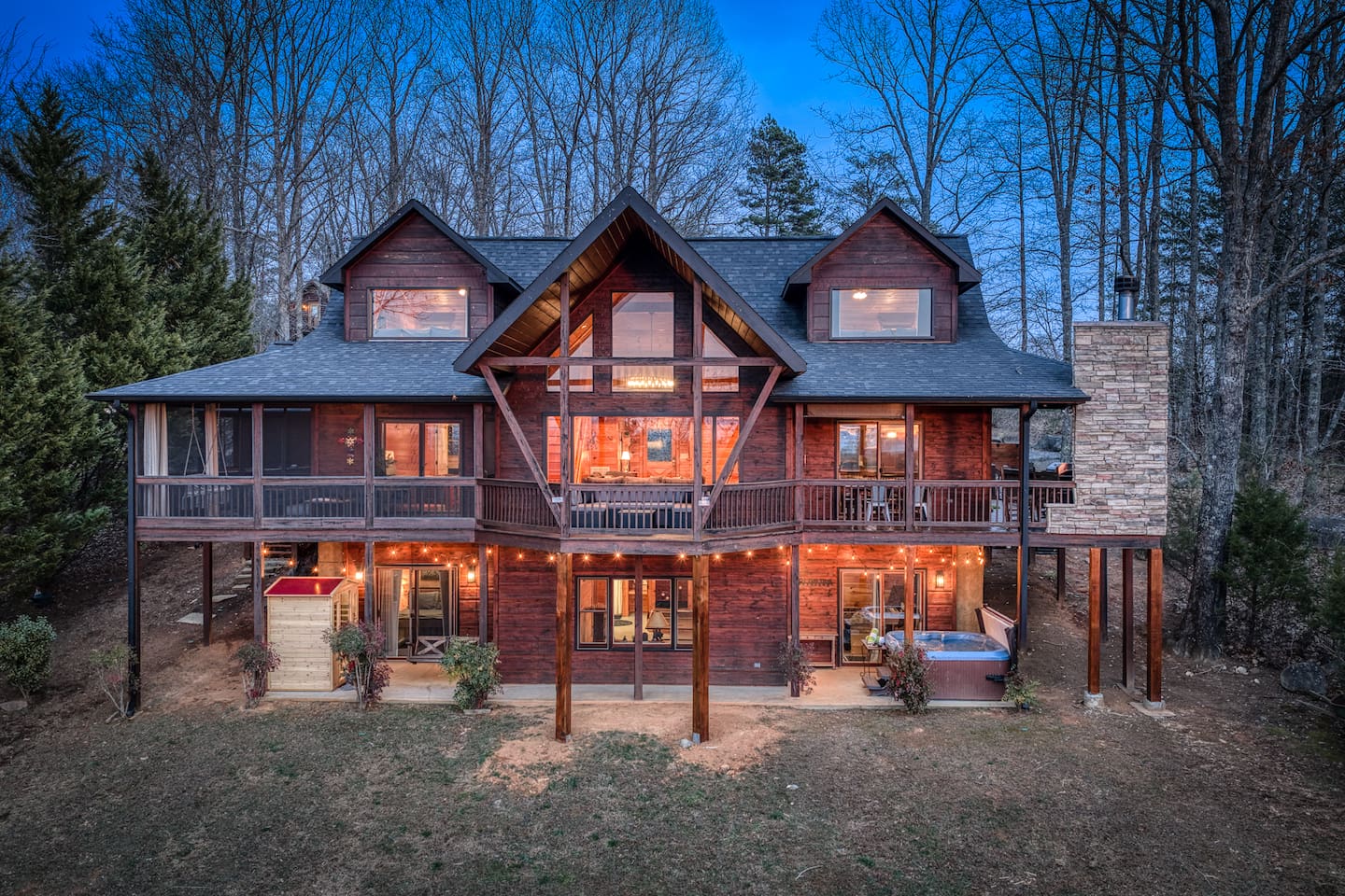 The back of the beautiful "Blessed Sunset" mountain retreat home overlooking the back yard! Stunning A-frame, wrap-around porch, screened-in patio, outdoor fireplace, outdoor dining table, sauna, hot tub, outdoor couch, and more!