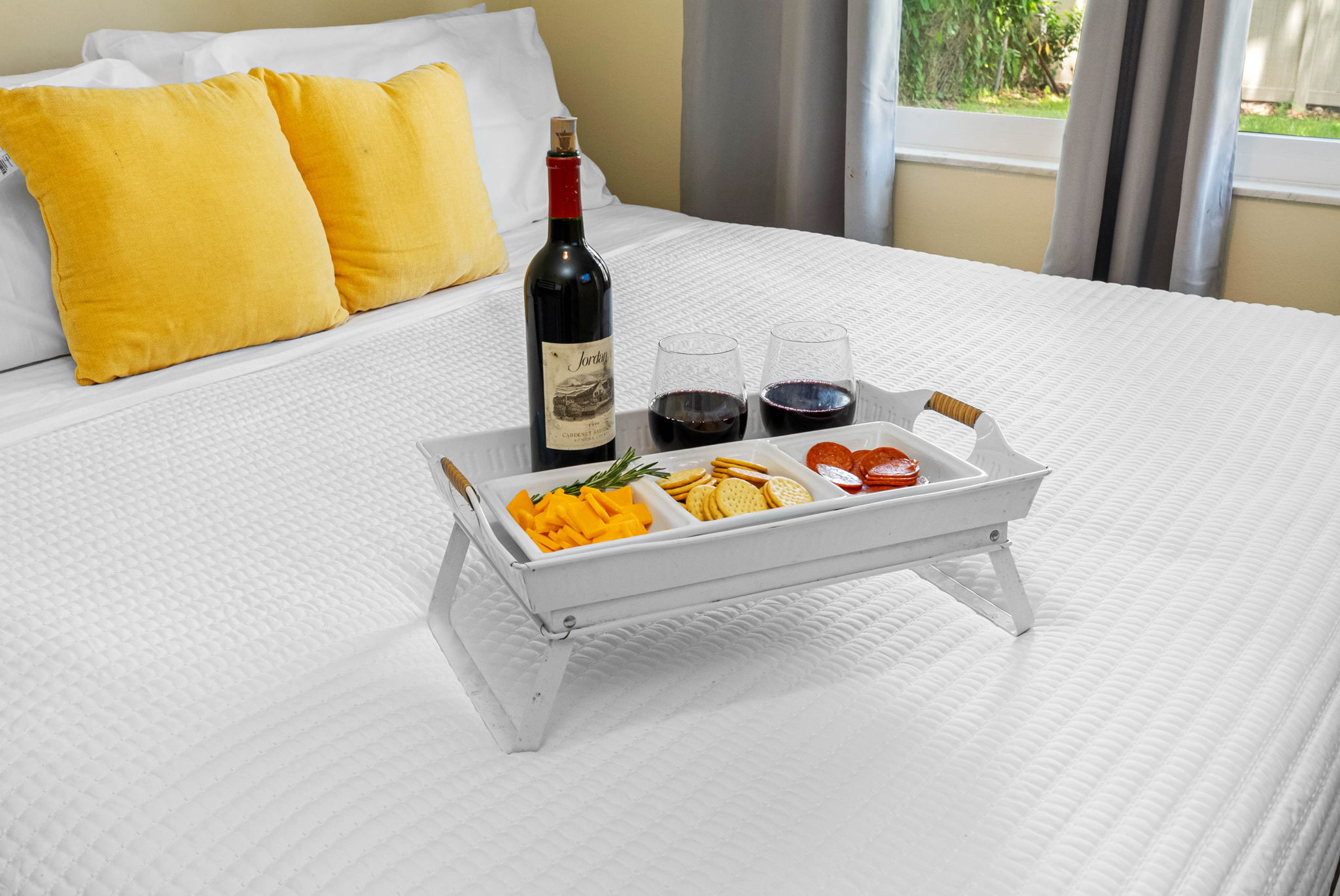 The centerpiece of the room is a luxurious king-size bed, dressed in crisp white linens and accented with vibrant yellow throw pillows for a cheerful pop of color and added comfort.