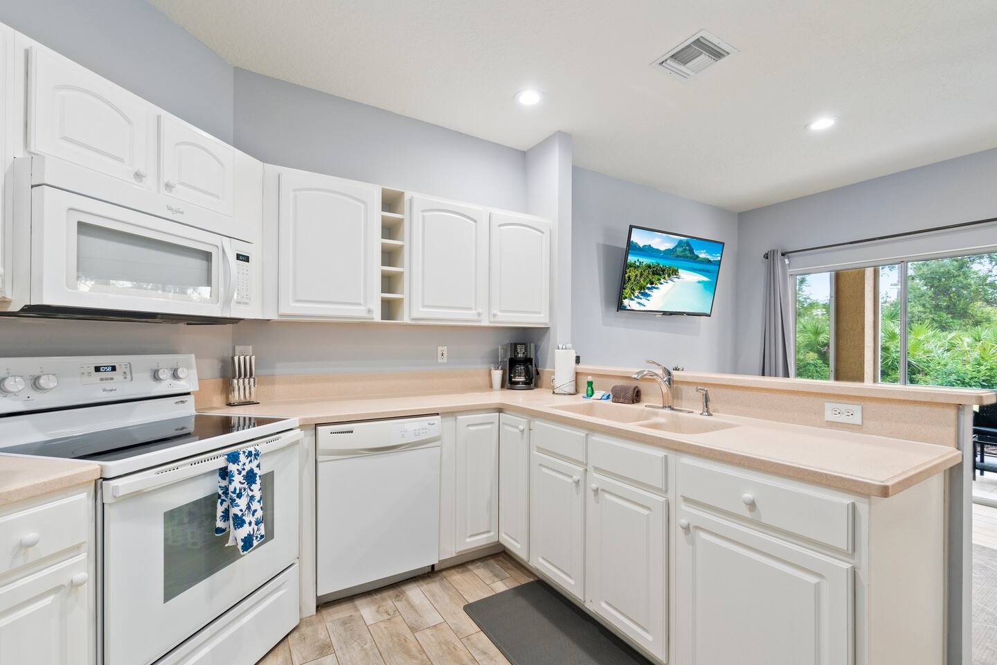 Bright kitchen with white cabinets, full-size appliances, breakfast bar, and an open view toward the living area.