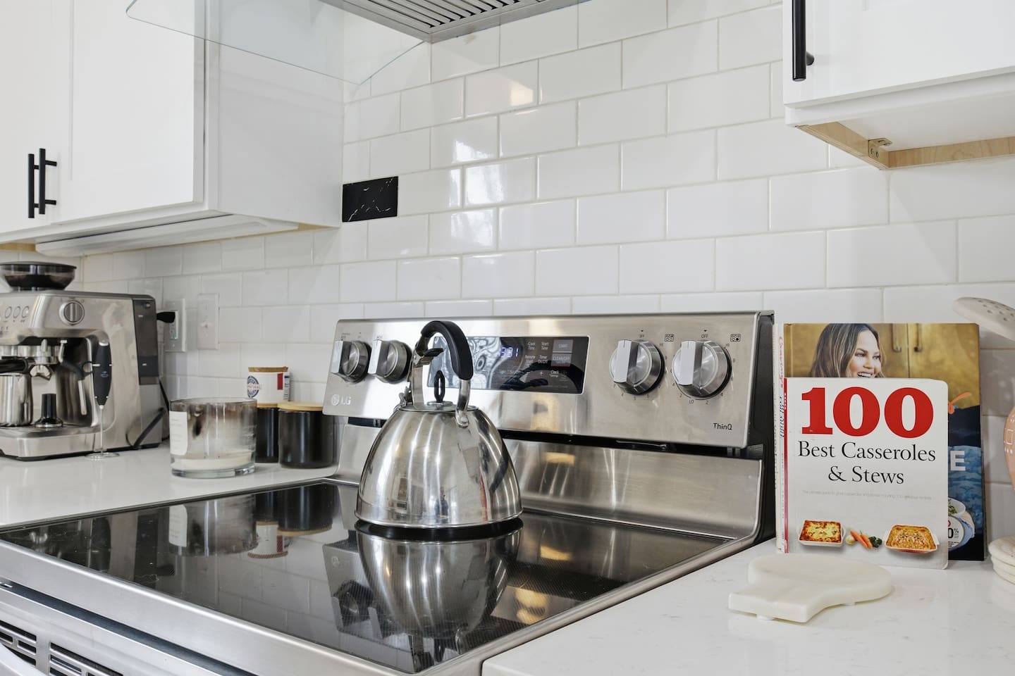Electric stovetop and oven with kettle, backsplash tile, and modern cooking setup.